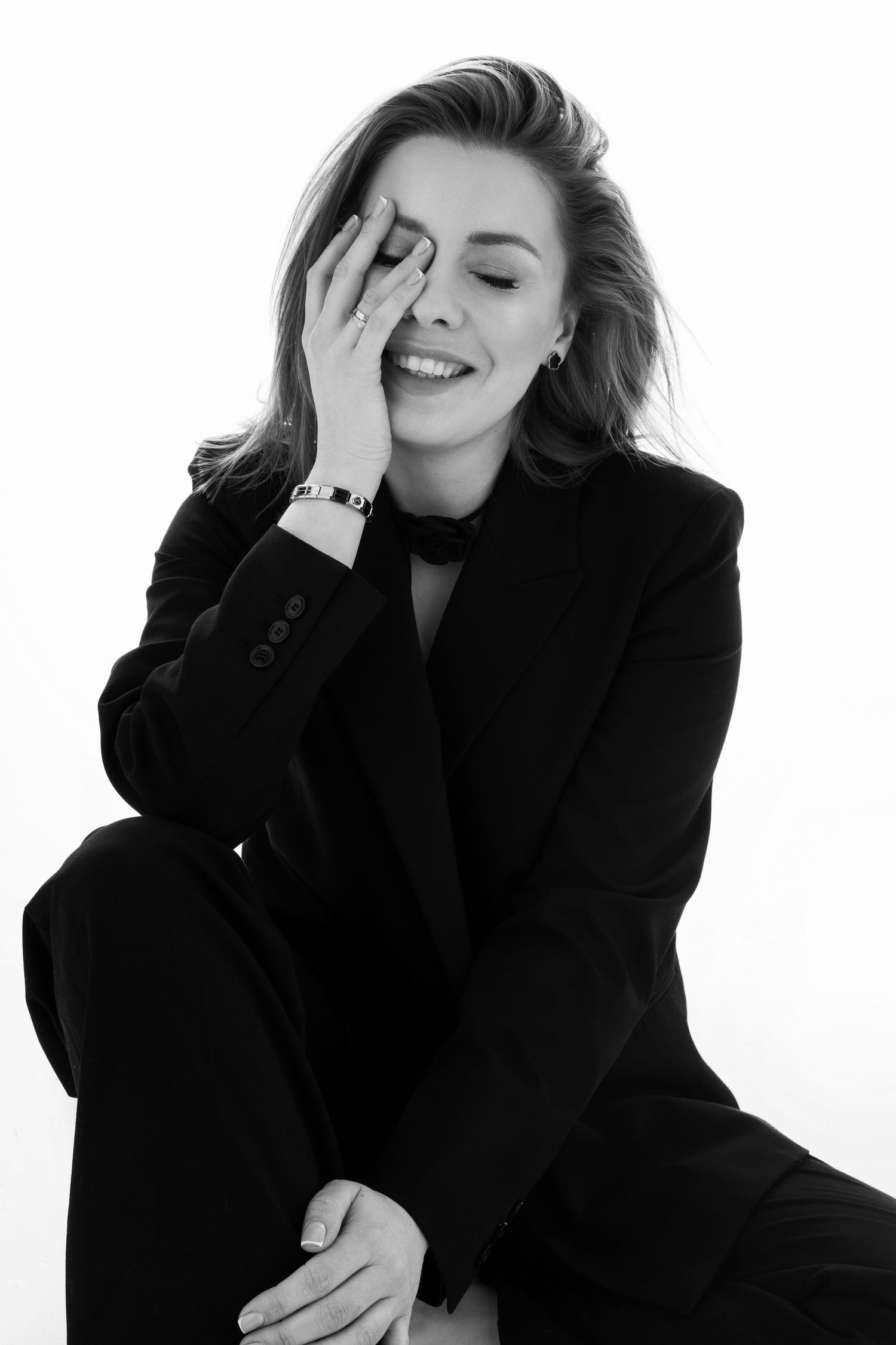 Black and white portrait of a woman in a blazer laughing with her hand on her face.