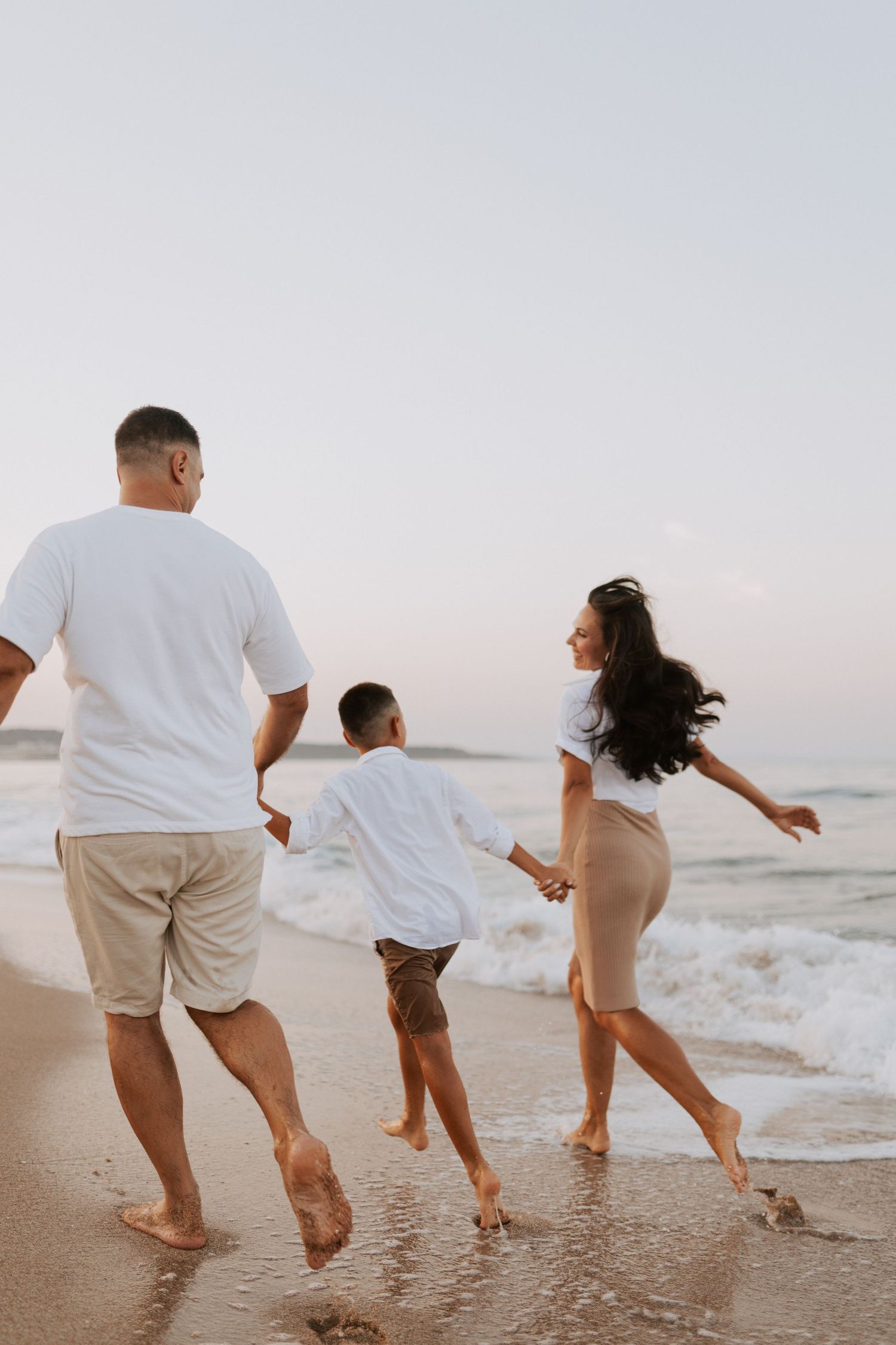 A family plays and jumps together at the water's edge on a sunset beach.