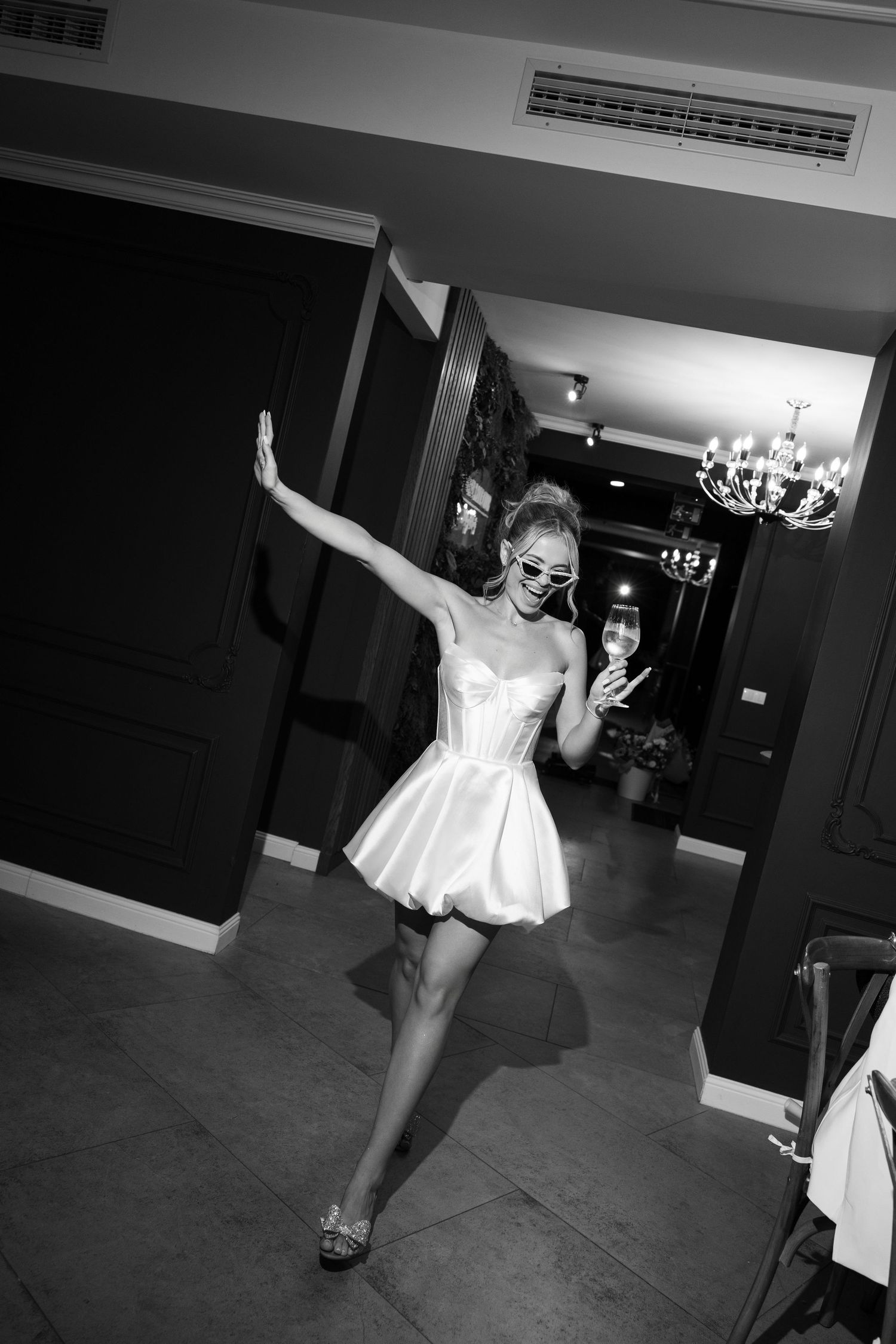 A dancer in a white dress performs expressive movements in a dimly lit studio space.