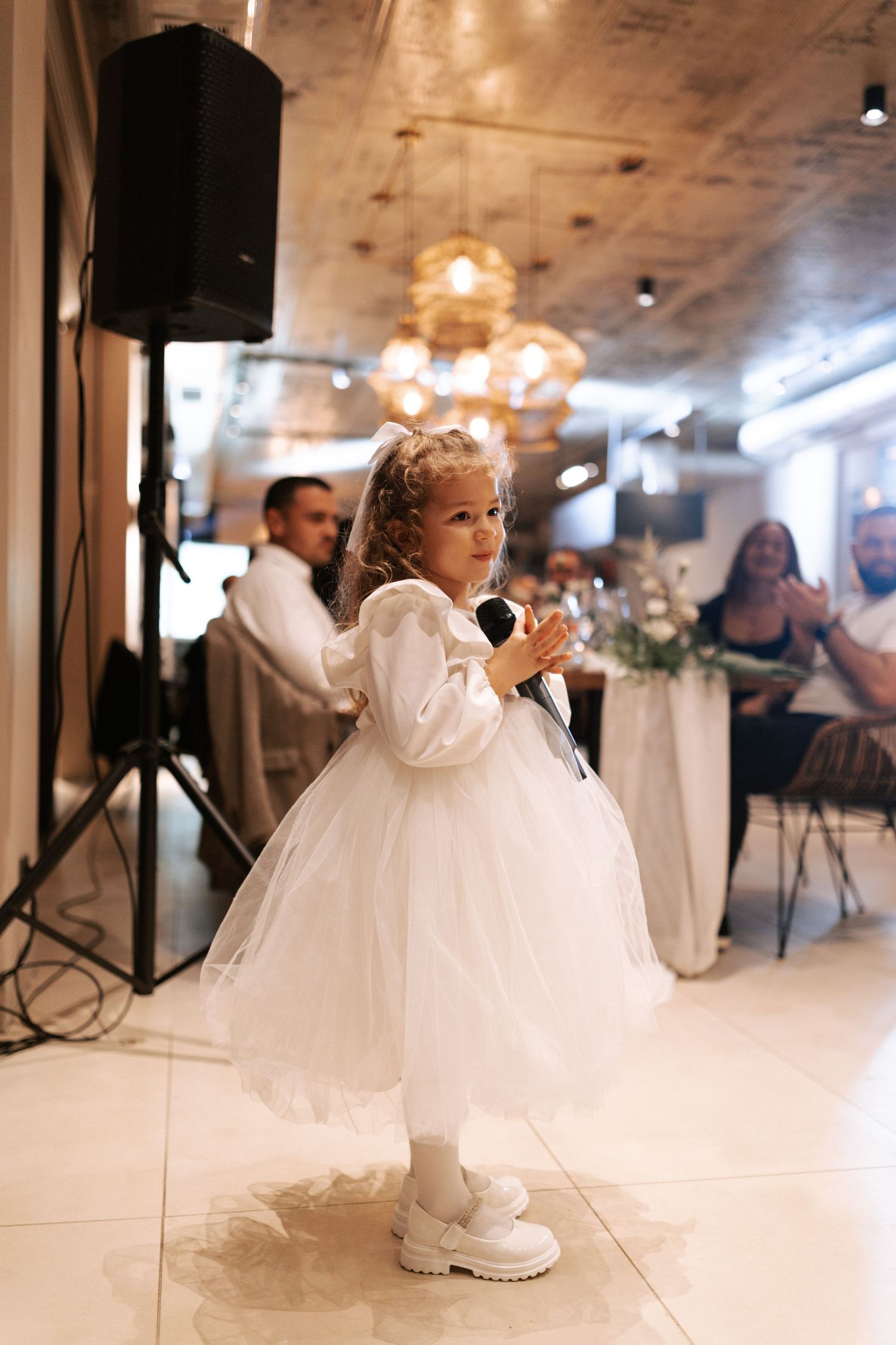 Young flower girl in white tulle dress and sneakers dancing at a wedding reception.
