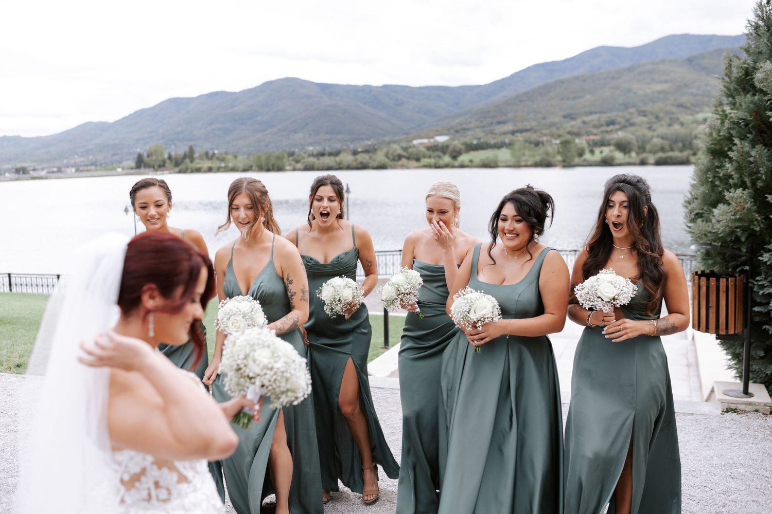 Joyful bridal party laughing together in matching sage gowns by the water.