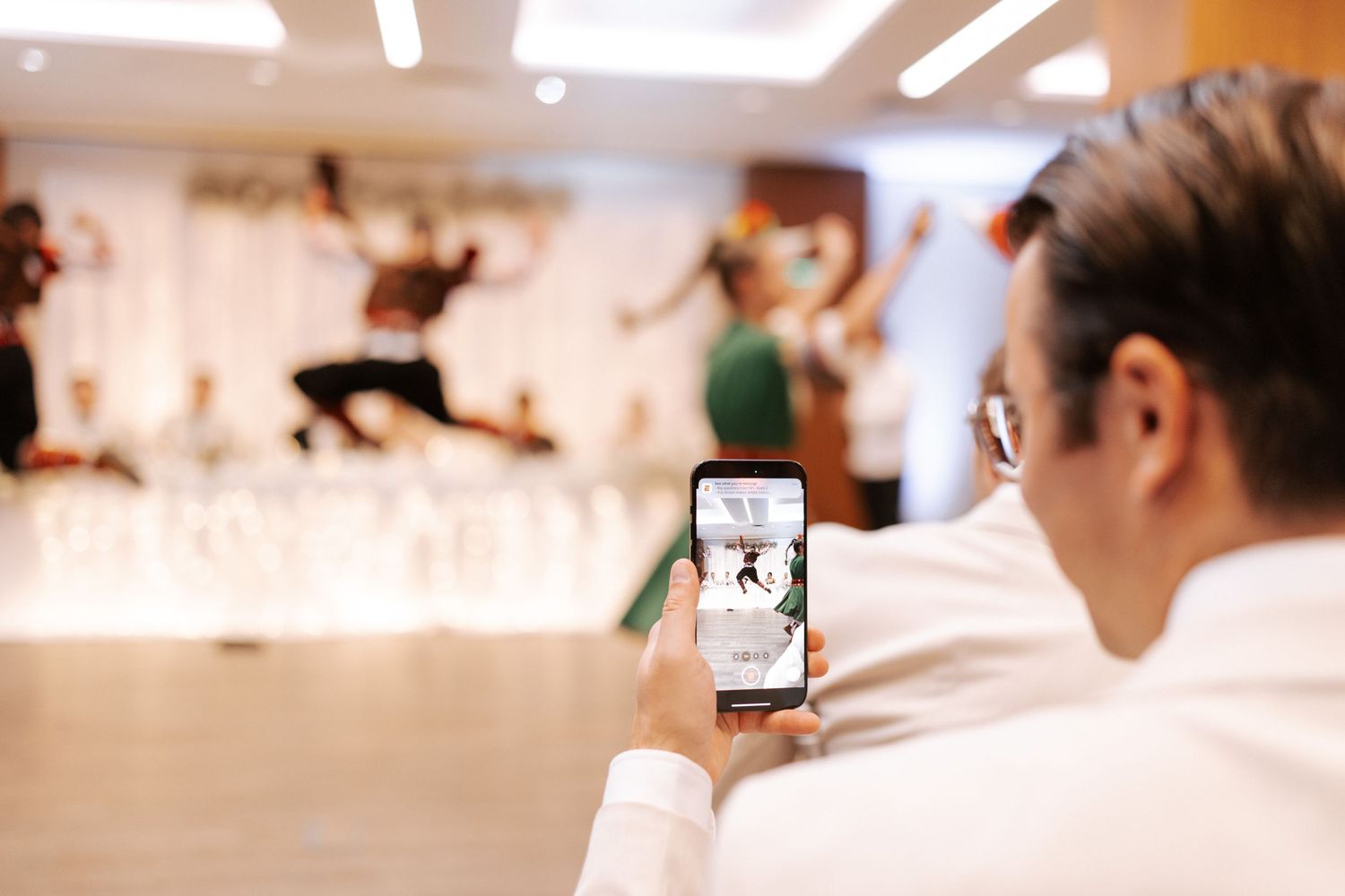 Guest captures dance performance on smartphone during wedding celebration.