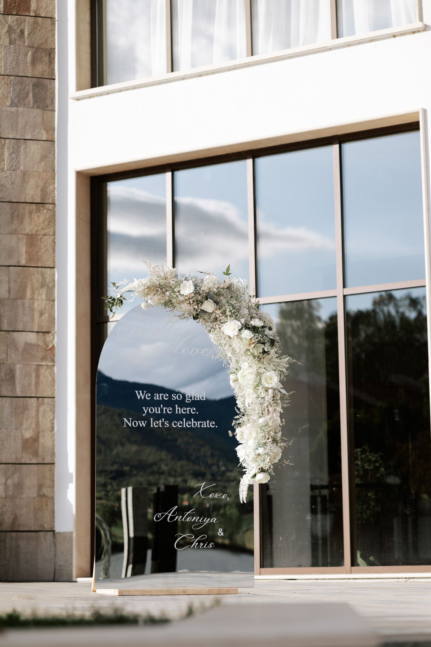 Modern building entrance decorated with white floral arch and welcome text on window.