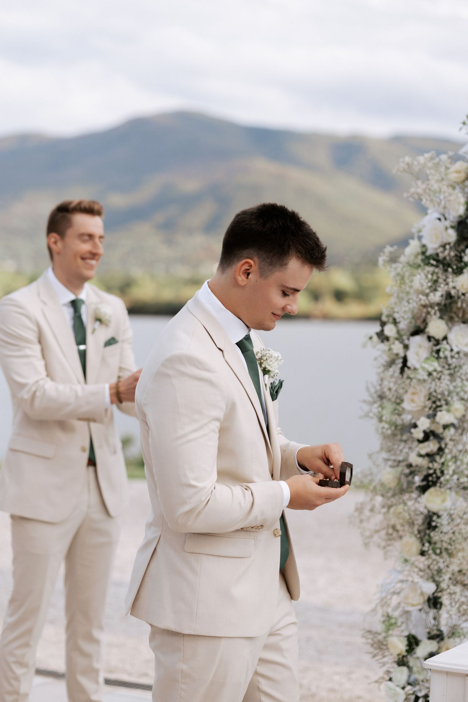 Groomsmen in cream-colored suits prepare during outdoor mountain wedding ceremony.