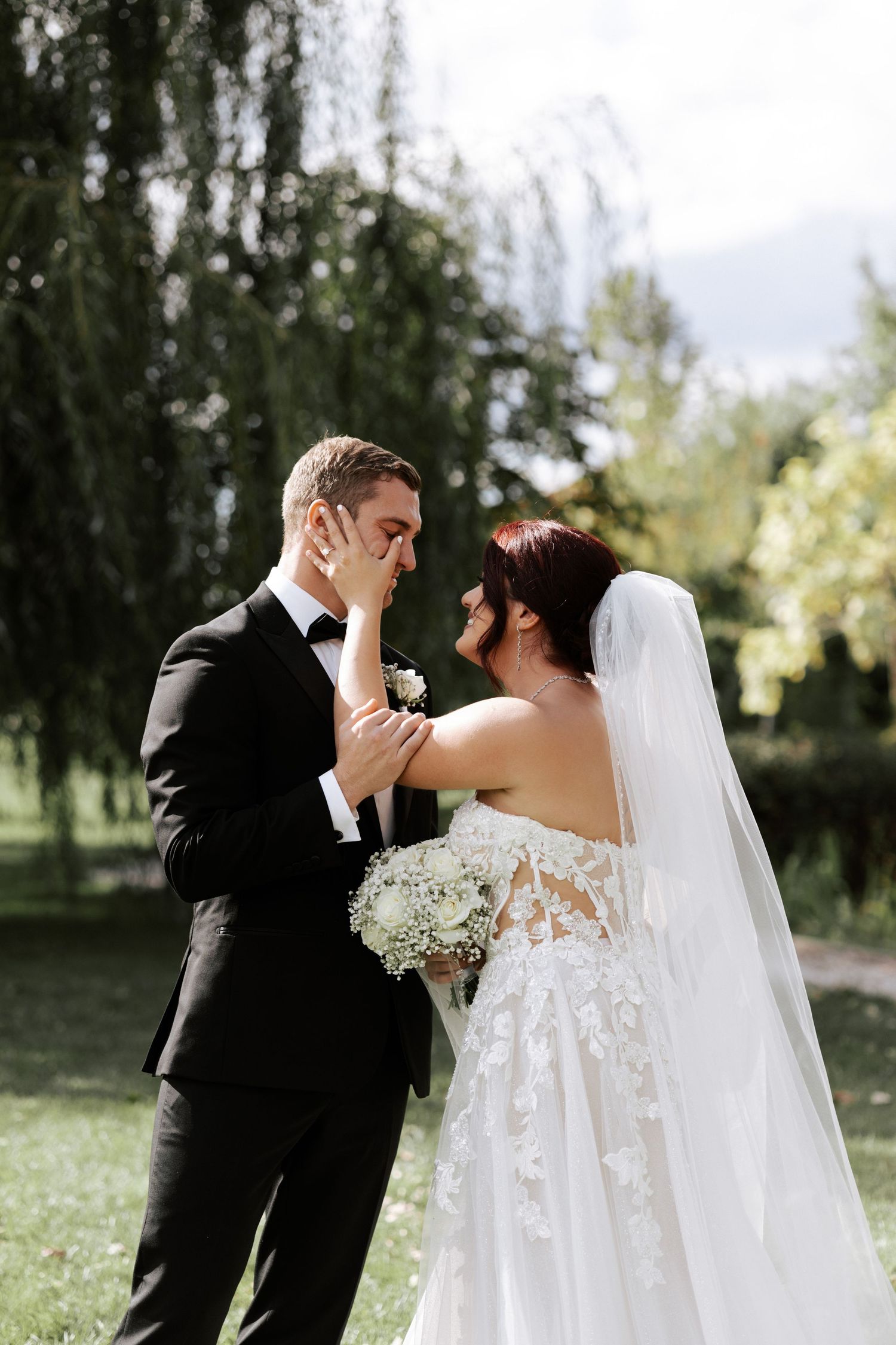 An emotional wedding moment captured under weeping willow trees in a garden setting.