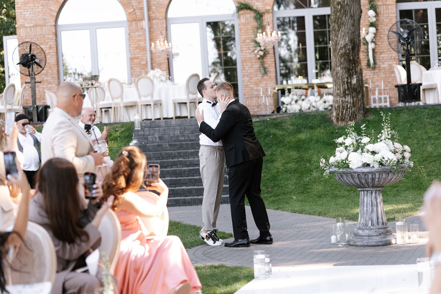 Guests mingling outside a brick venue with arched windows during a formal event.