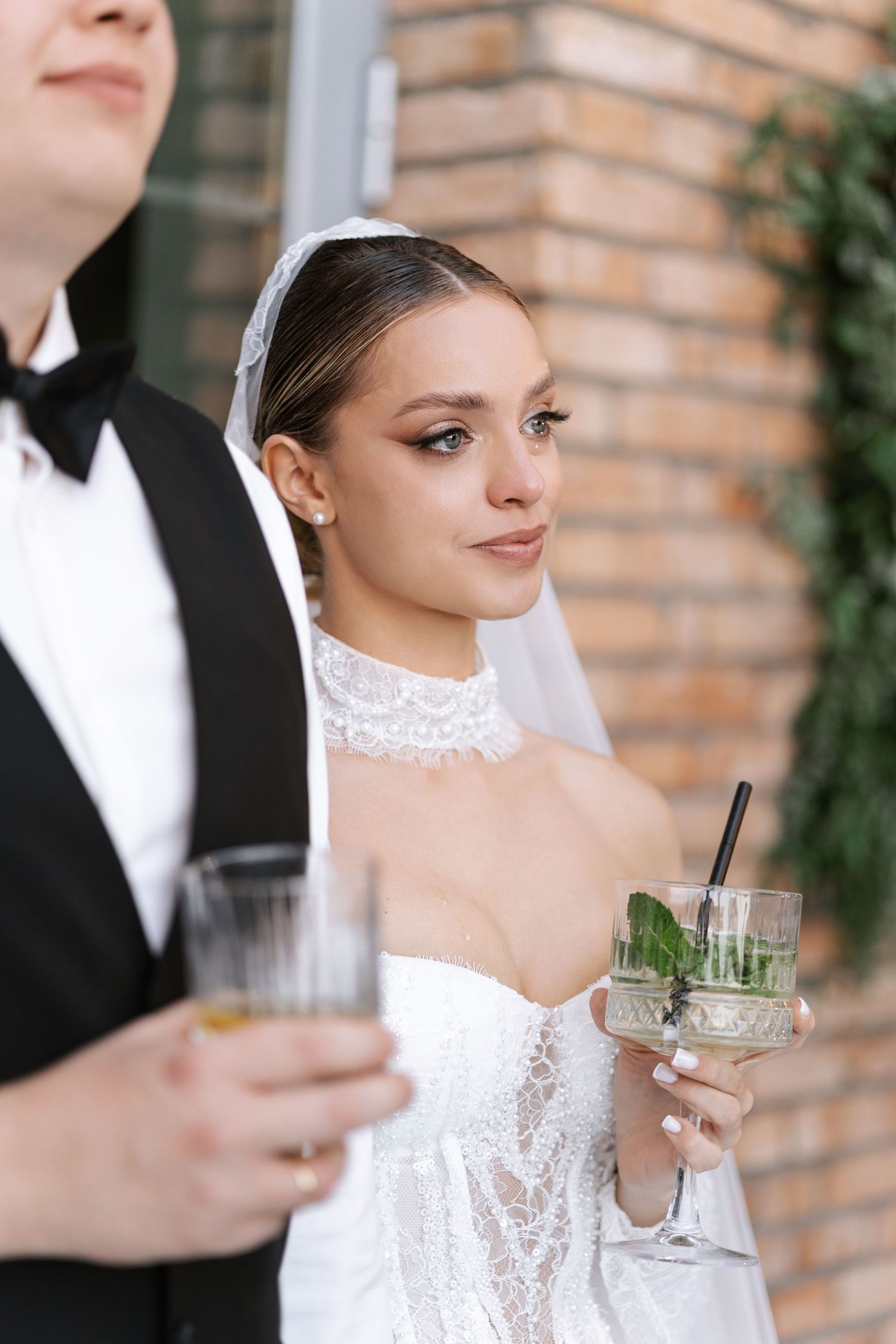 Bride in lace dress and groom hold cocktails during wedding celebration.