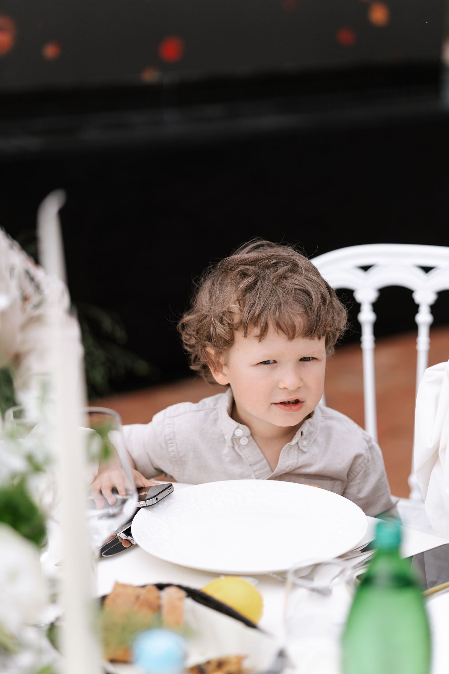 A child in a white shirt sits at an elegant table setting with white chairs and dishes.