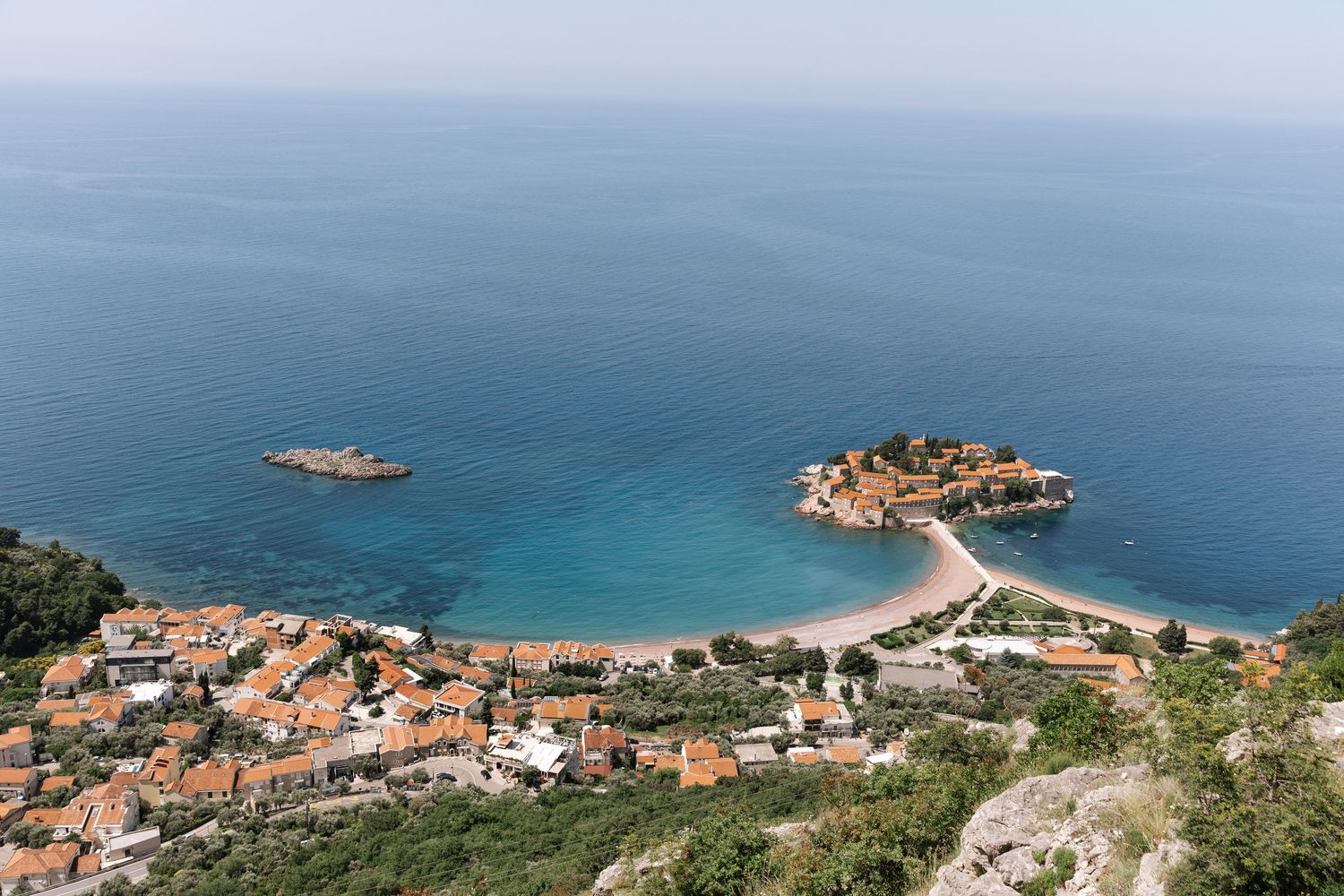 Aerial panoramic view of coastal Mediterranean town with red rooftops and turquoise waters along rocky shoreline.