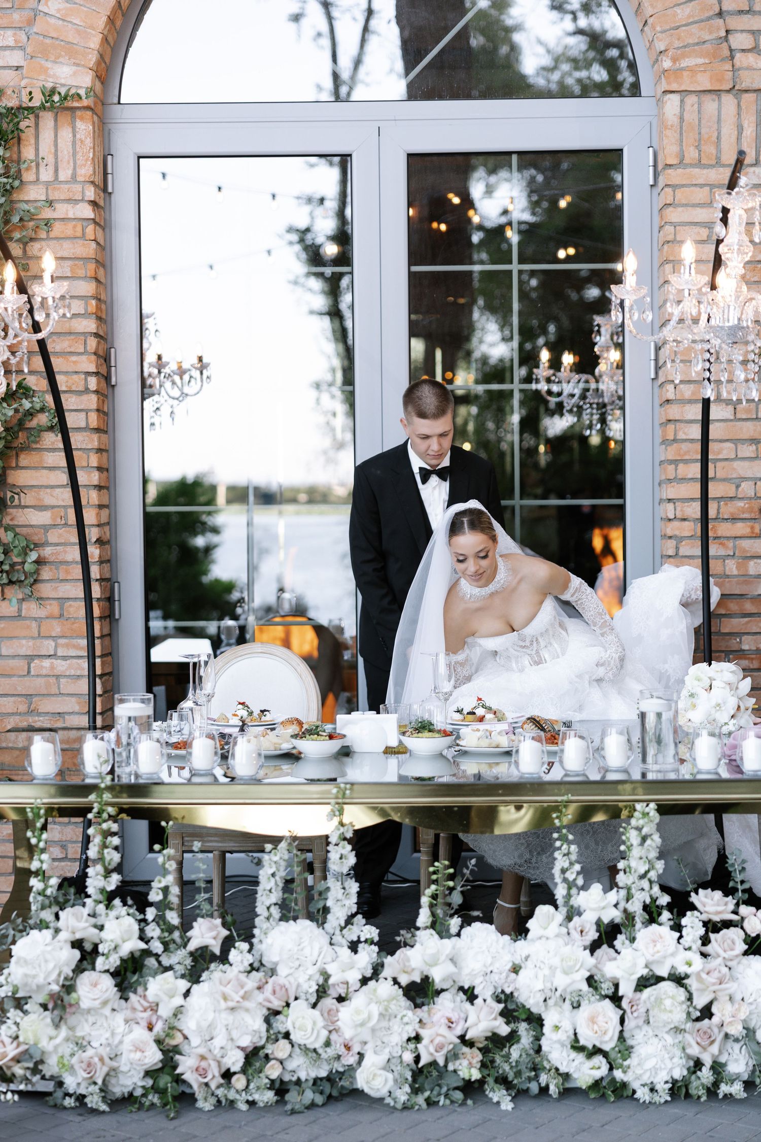 Wedding reception setup with white floral arrangements along windowsills of a brick building.
