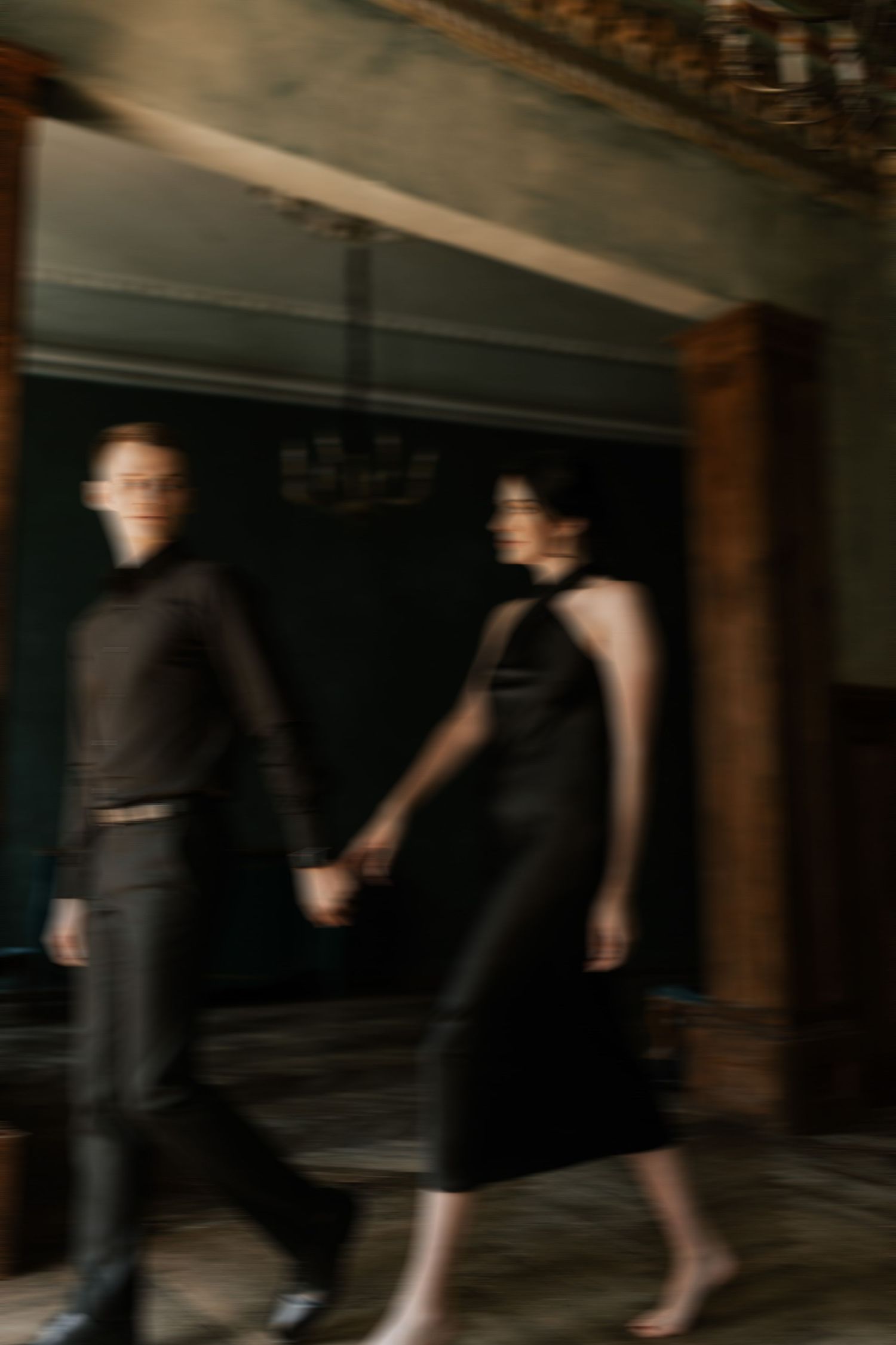Blurred motion shot of couple walking hand in hand through elegant room with ornate ceiling.