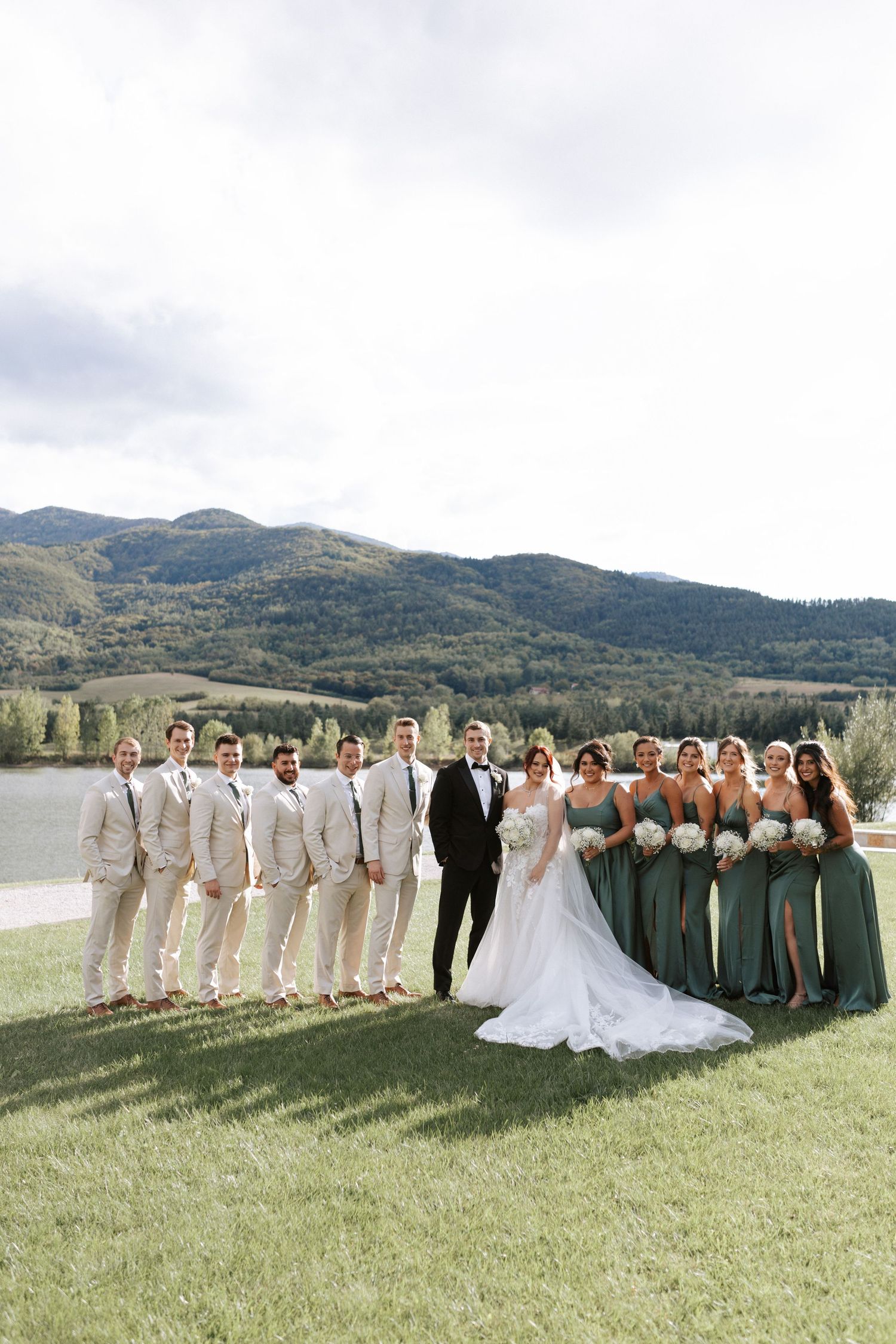 Wedding party in sage green and beige poses with scenic mountain backdrop.