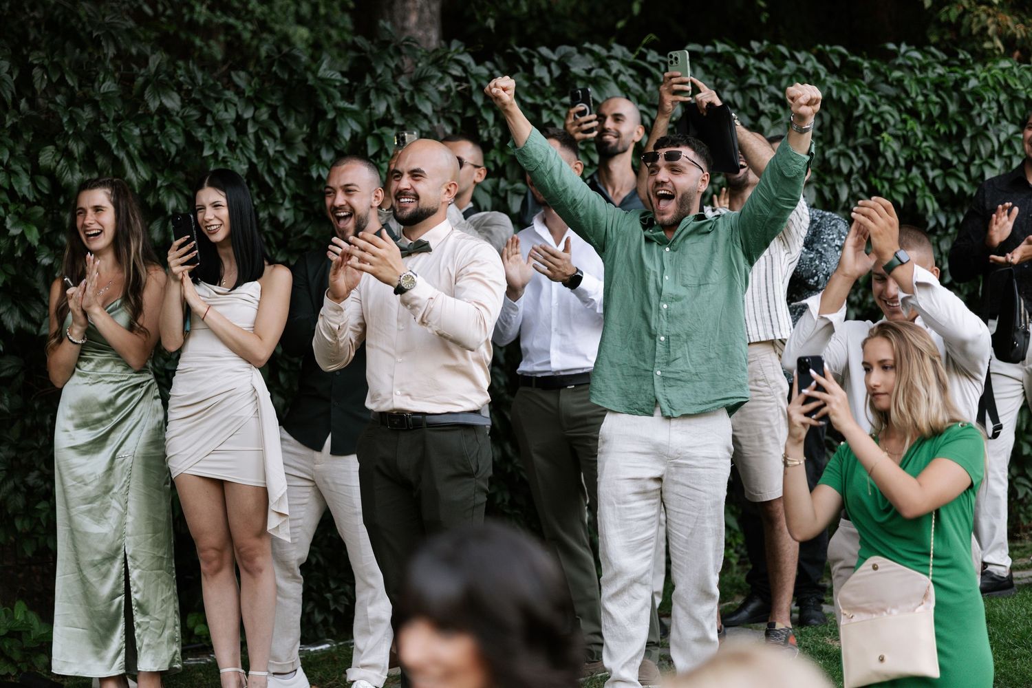 Wedding guests in green and white attire dance and celebrate during an outdoor reception.