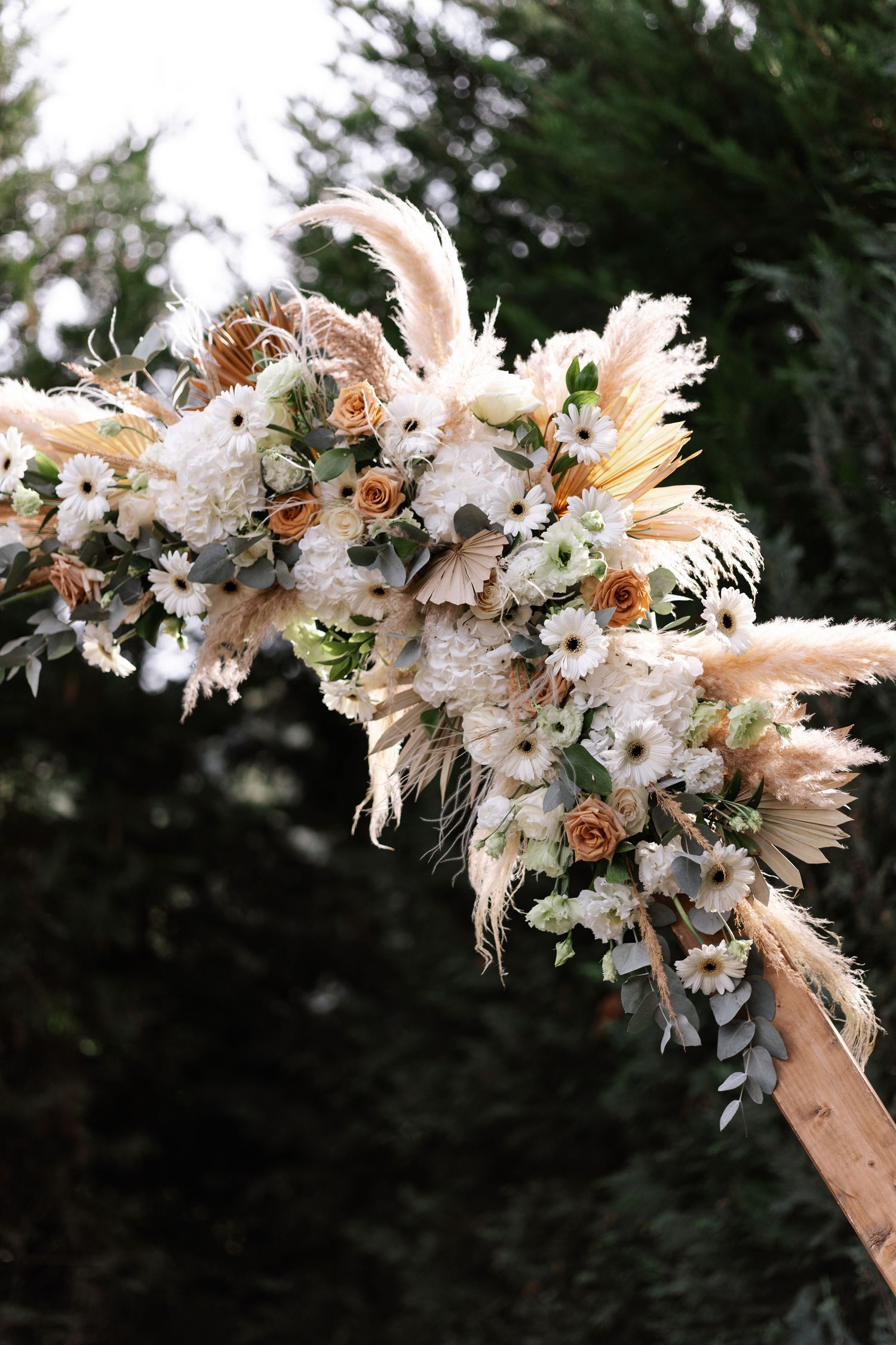 A curved floral installation with white blooms and dried elements creates an ethereal arch against a dark background.
