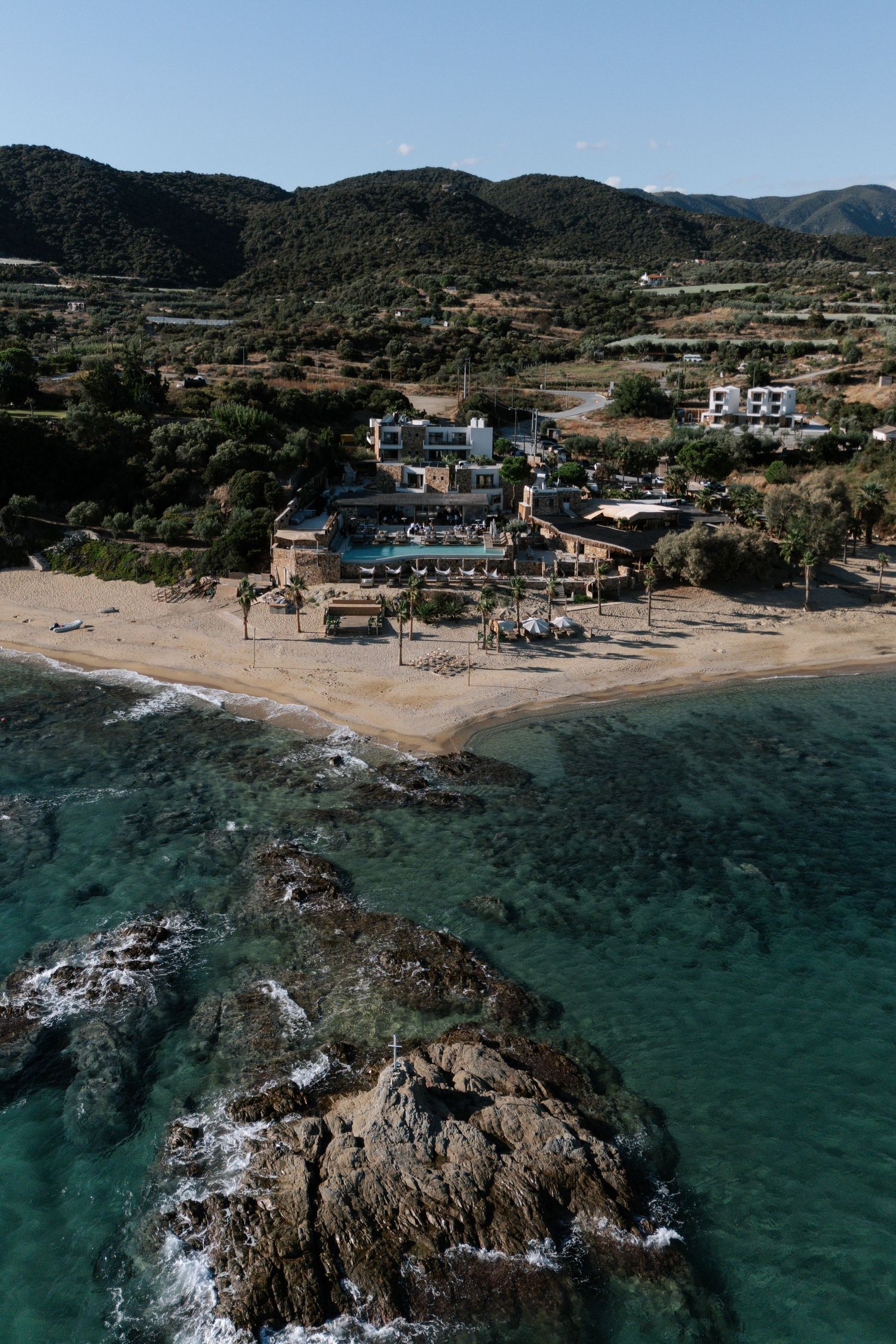 Aerial view of a coastal resort with turquoise waters, rocky outcrops, and Mediterranean buildings along the shoreline.