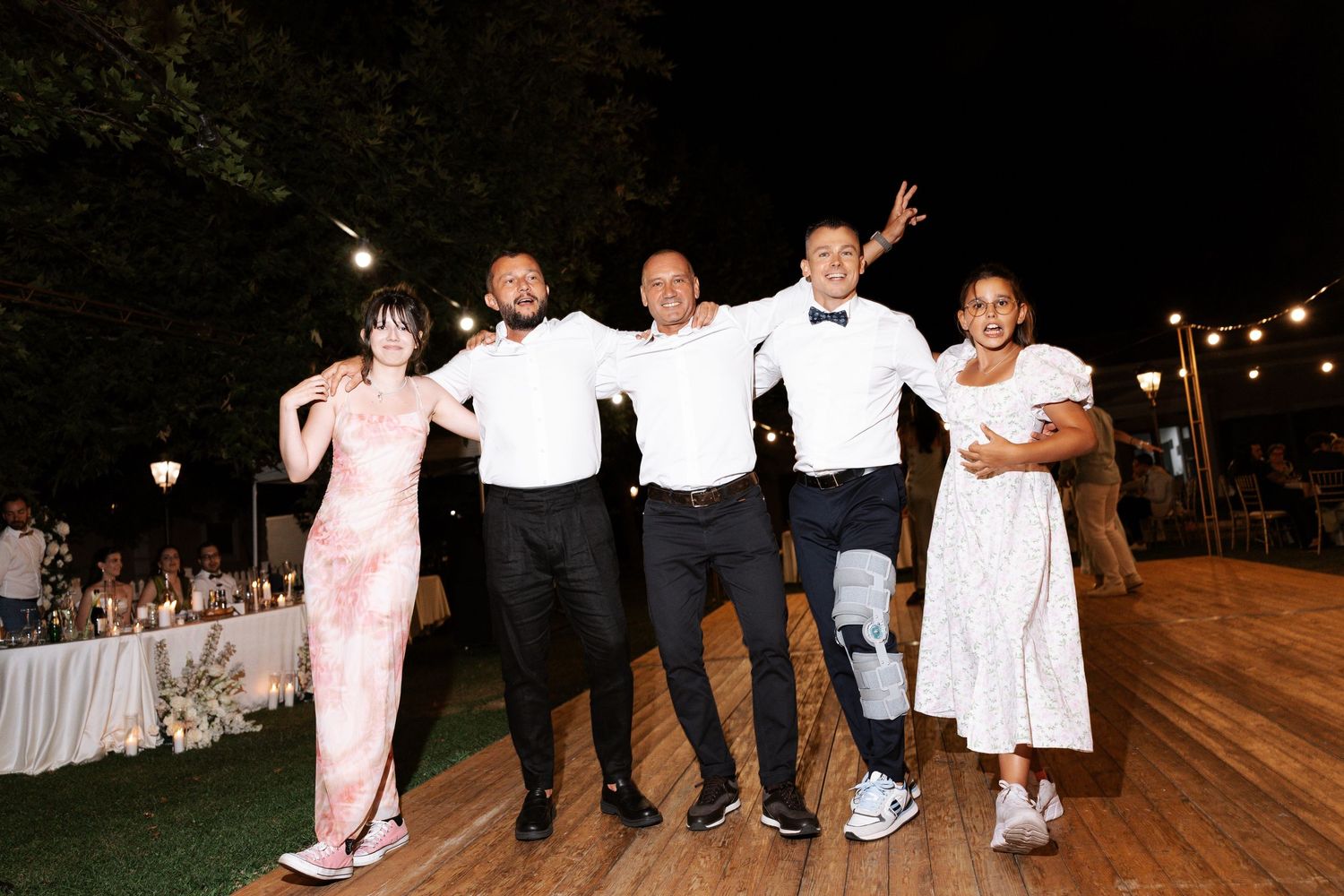People dancing and celebrating on a wooden dance floor at an outdoor evening wedding reception.