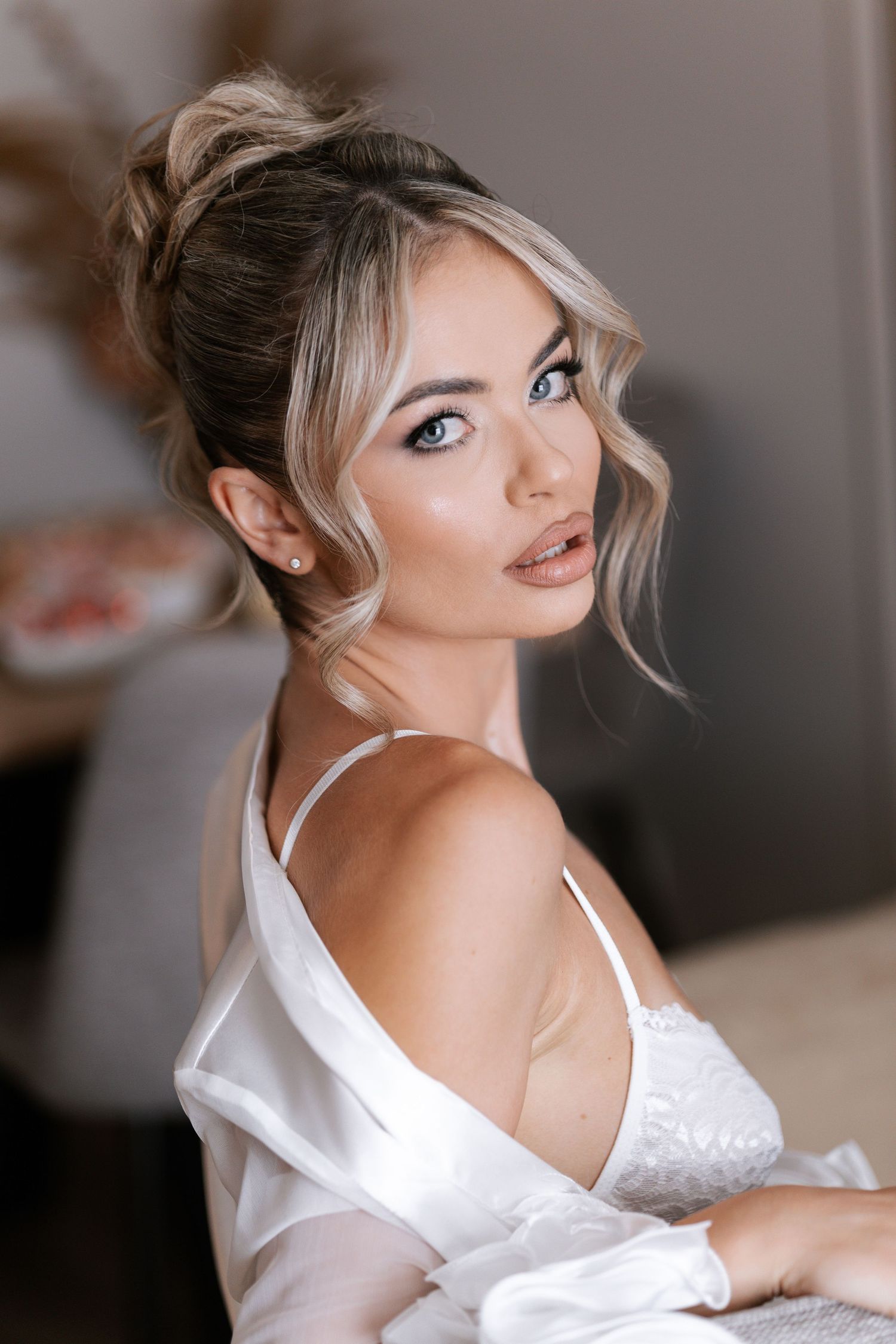 Portrait of a woman with blonde hair in an updo wearing a white silk robe and lingerie in soft lighting.