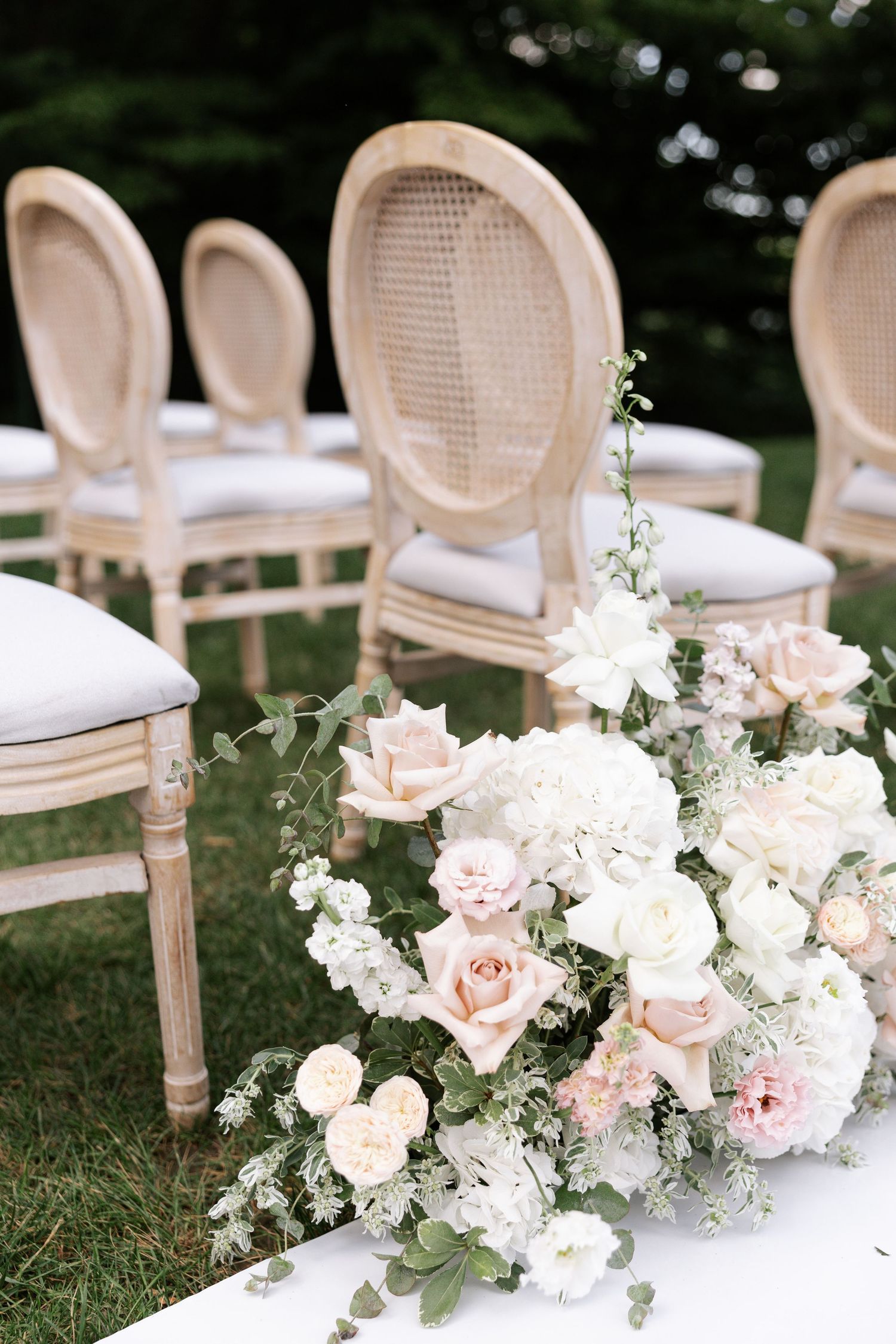 Elegant outdoor wedding setup with white French country chairs and pink floral arrangements.