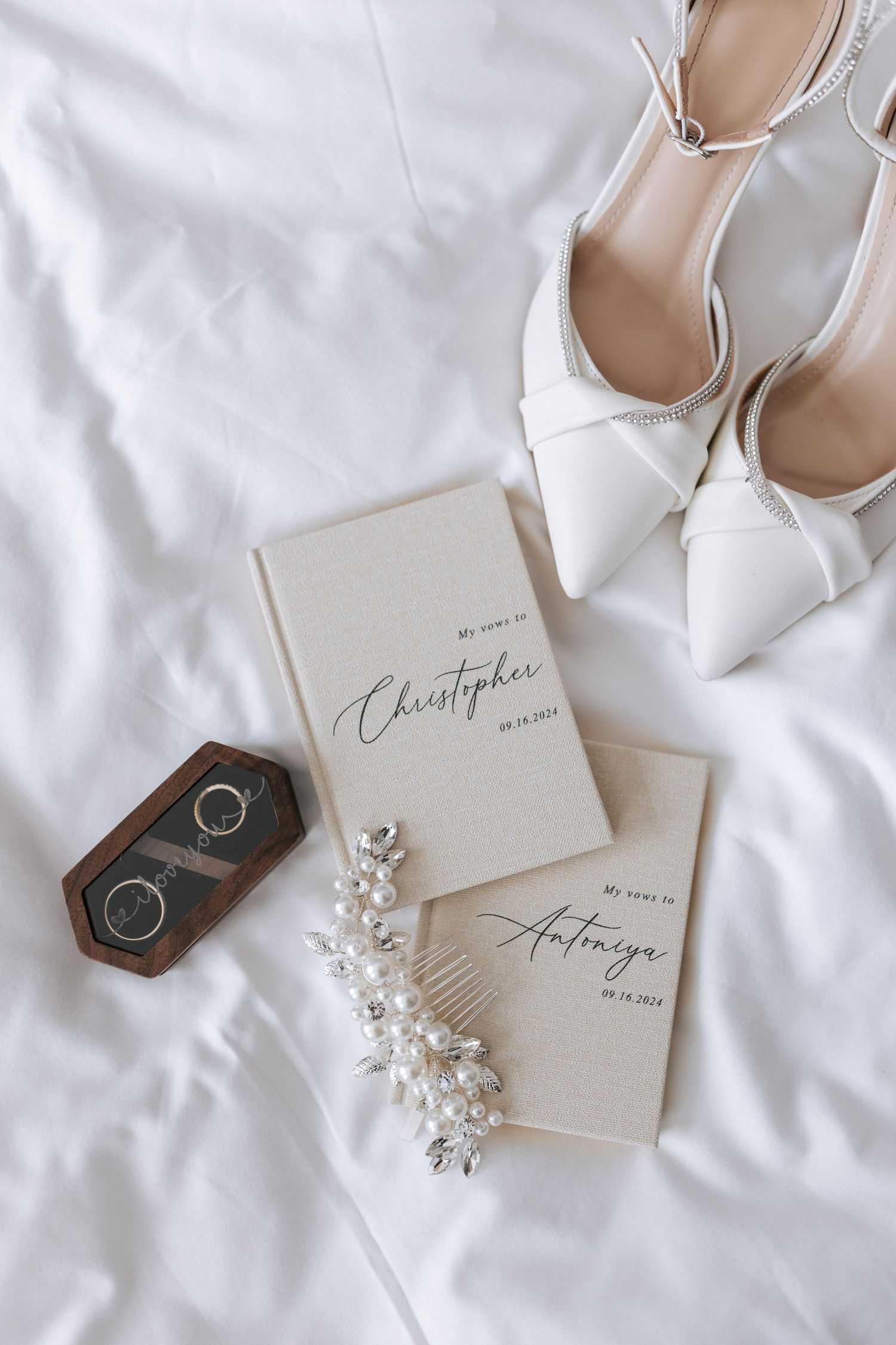 White bridal shoes, vow books and wedding rings styled with baby's breath on white fabric.