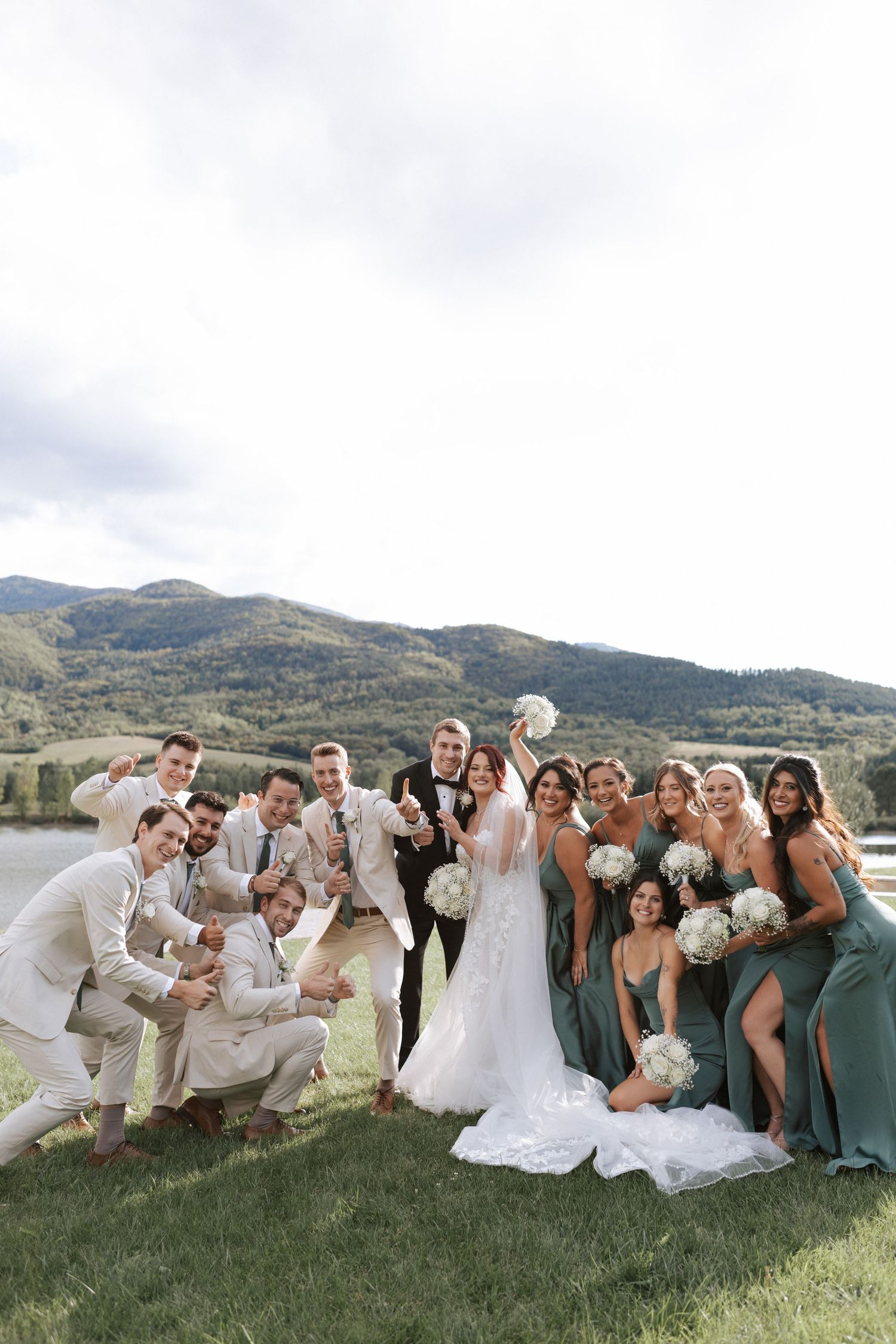 Joyful wedding party celebrates on hillside with mountain views.