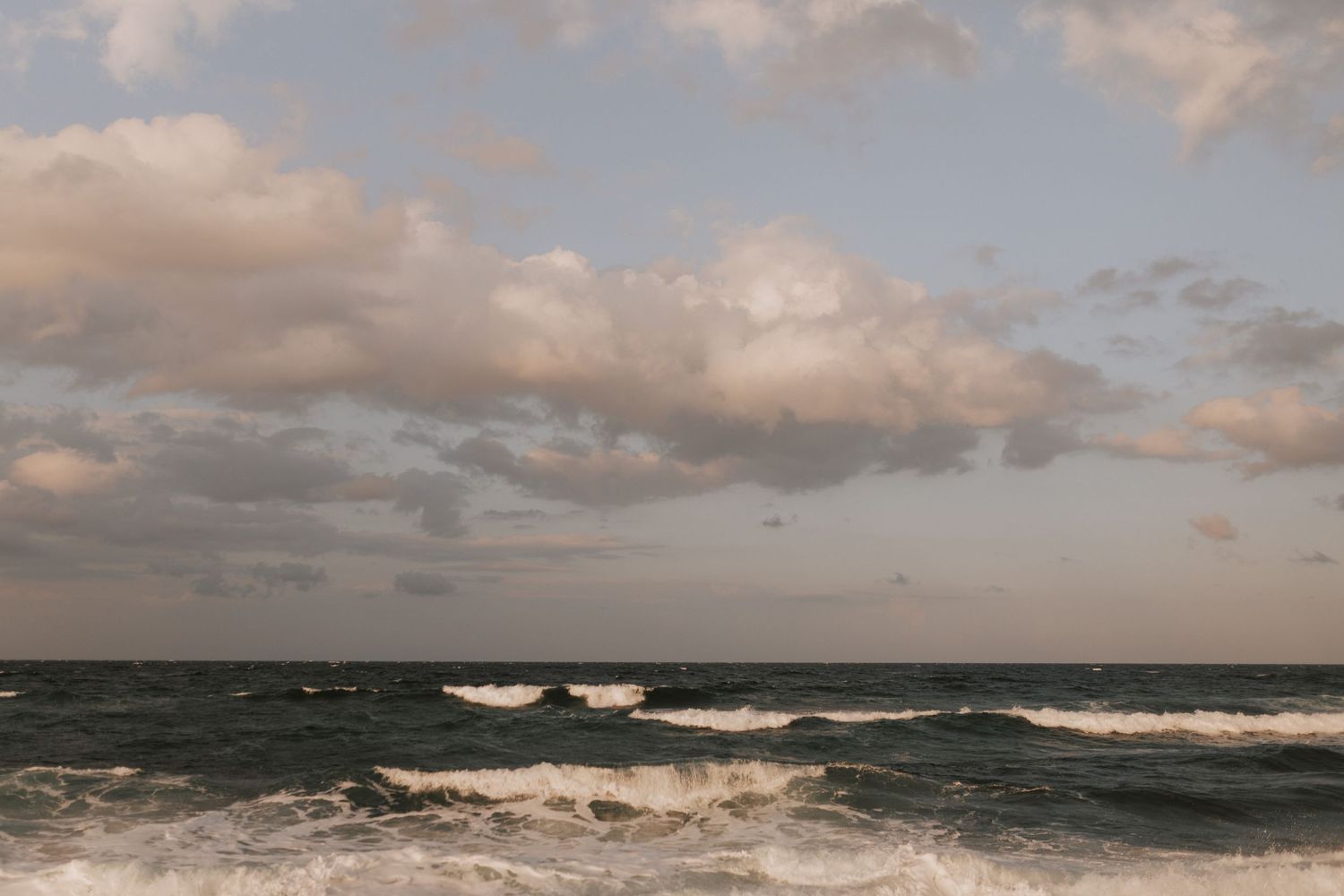 Dramatic seascape with rolling waves and warm sunset clouds over the ocean.