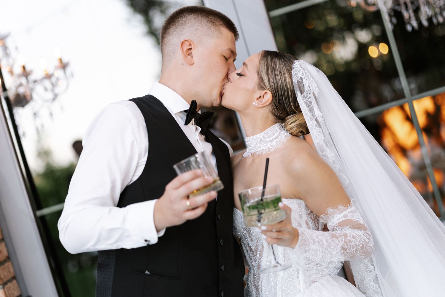 A couple in wedding attire shares drinks and a romantic moment during their celebration.