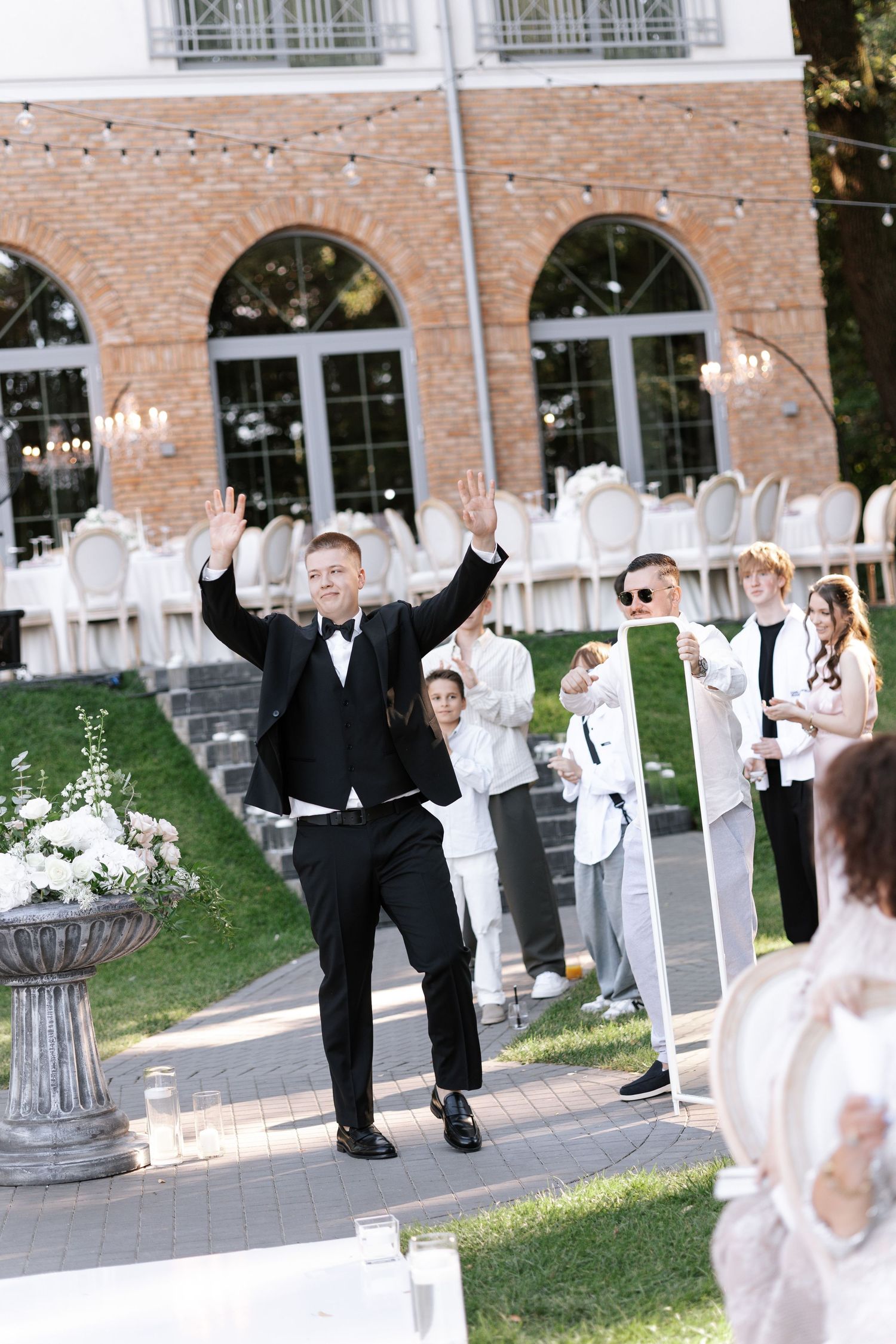 Wedding party members in formal attire celebrating on a brick-lined pathway.