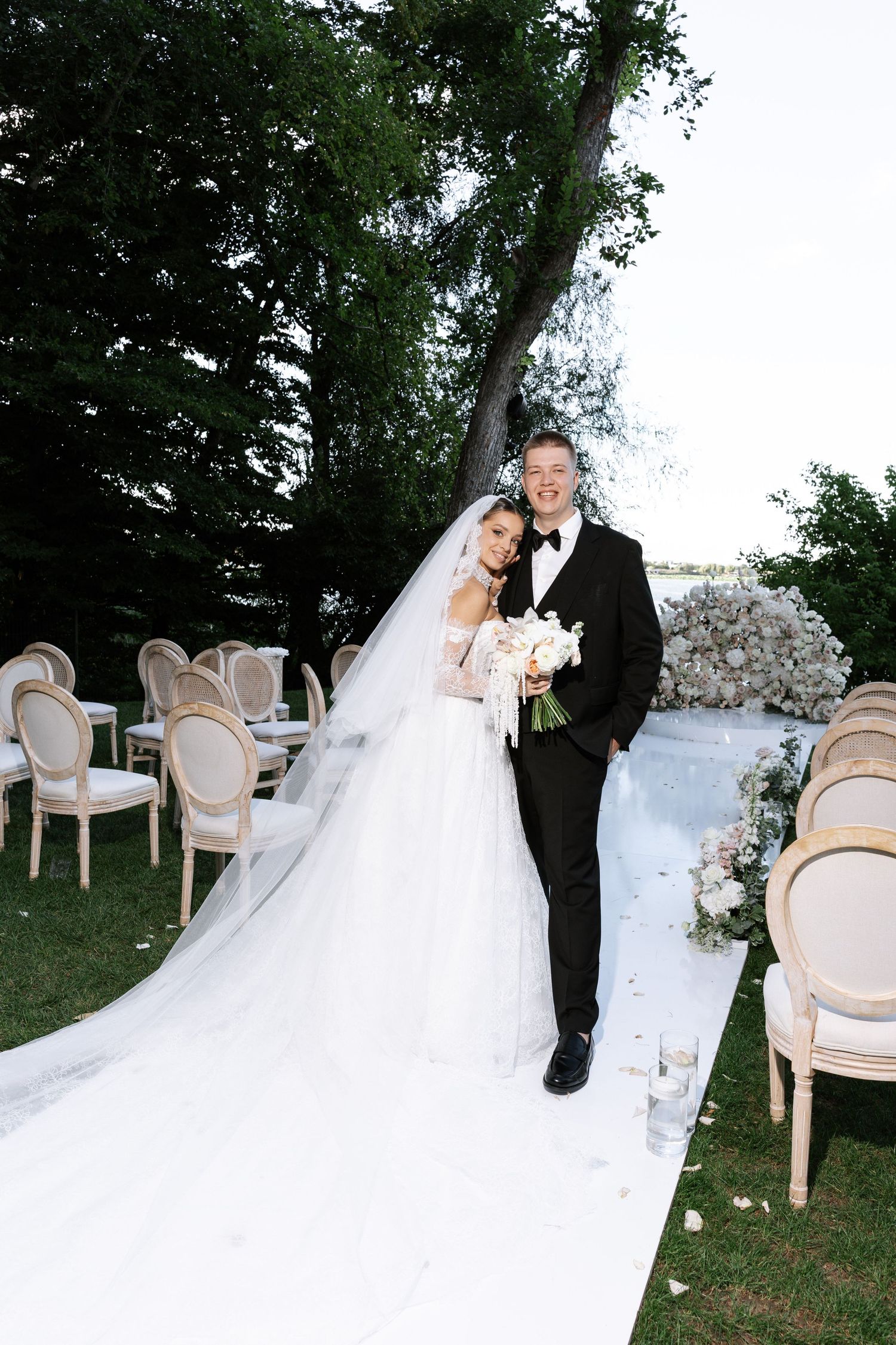 Romantic wedding portraits on a lawn with elegant cream-colored chairs and floral arrangements.
