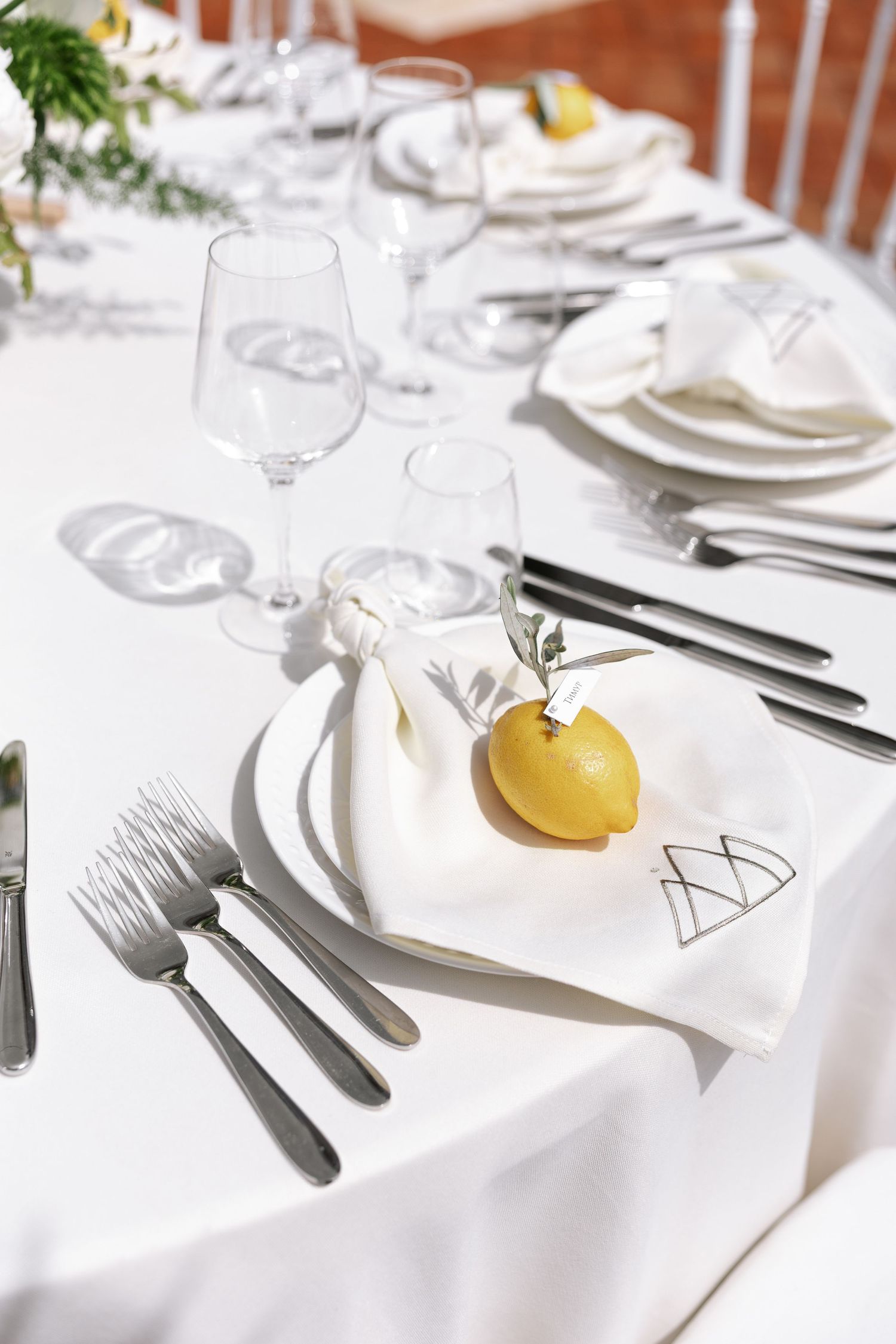 Elegant white table setting with yellow citrus garnish and polished silverware against a crisp white tablecloth.