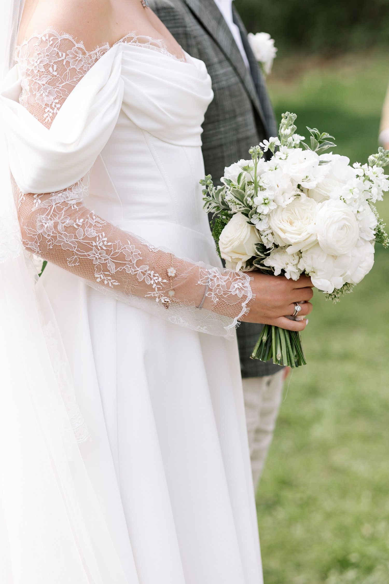 Close-up view of a white bridal bouquet with delicate lace details on the wedding dress sleeve.