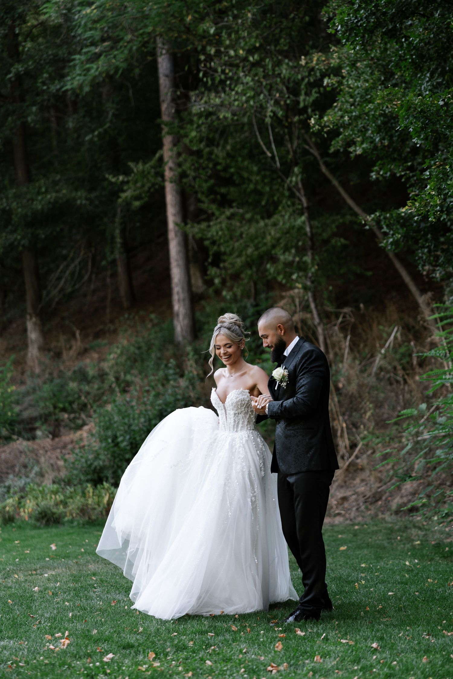 A couple shares a joyful moment on their wedding day, surrounded by lush green forest scenery.