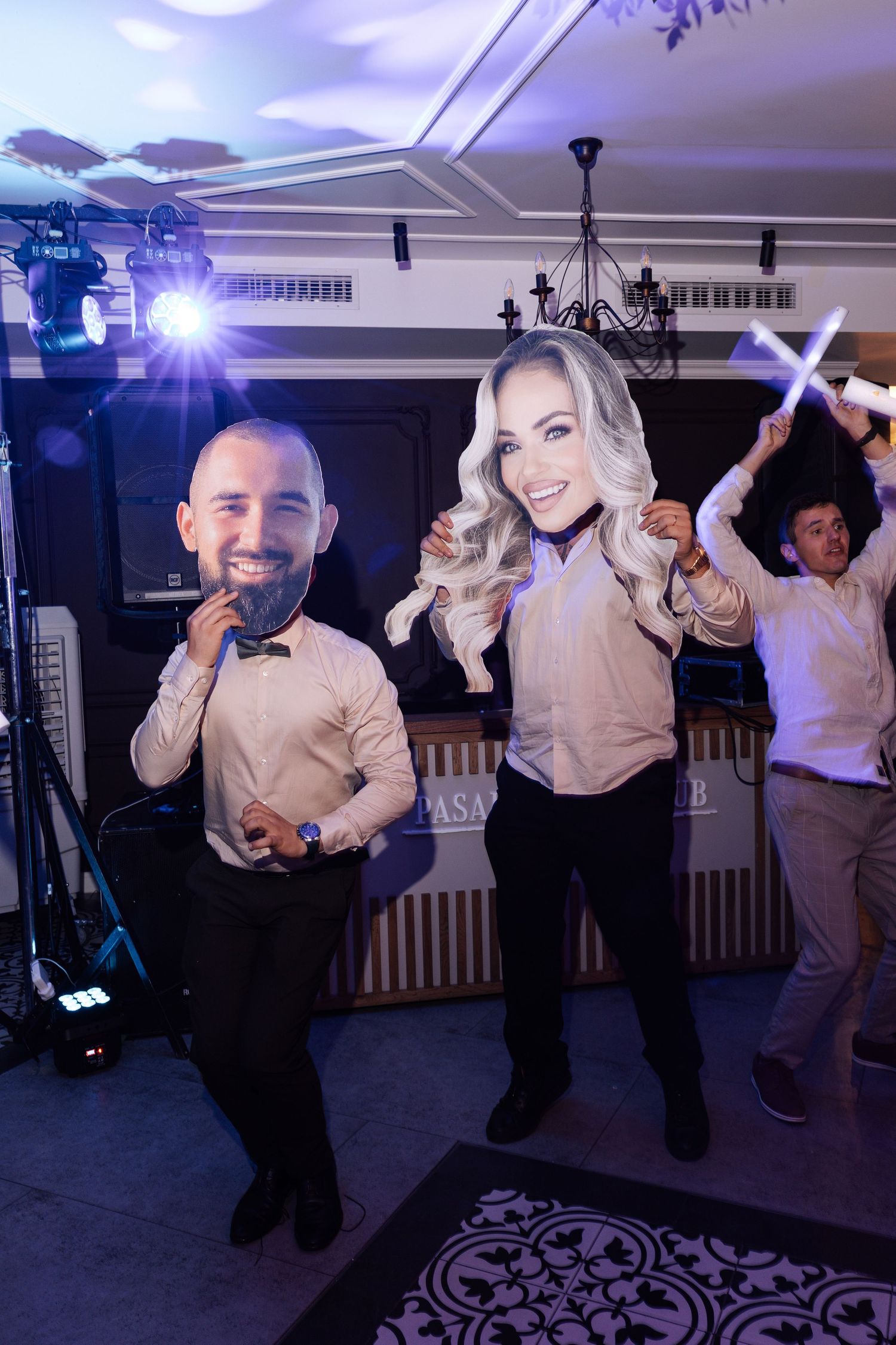 Wedding guests dance energetically on a dark dance floor with purple lighting and white ceiling decor.