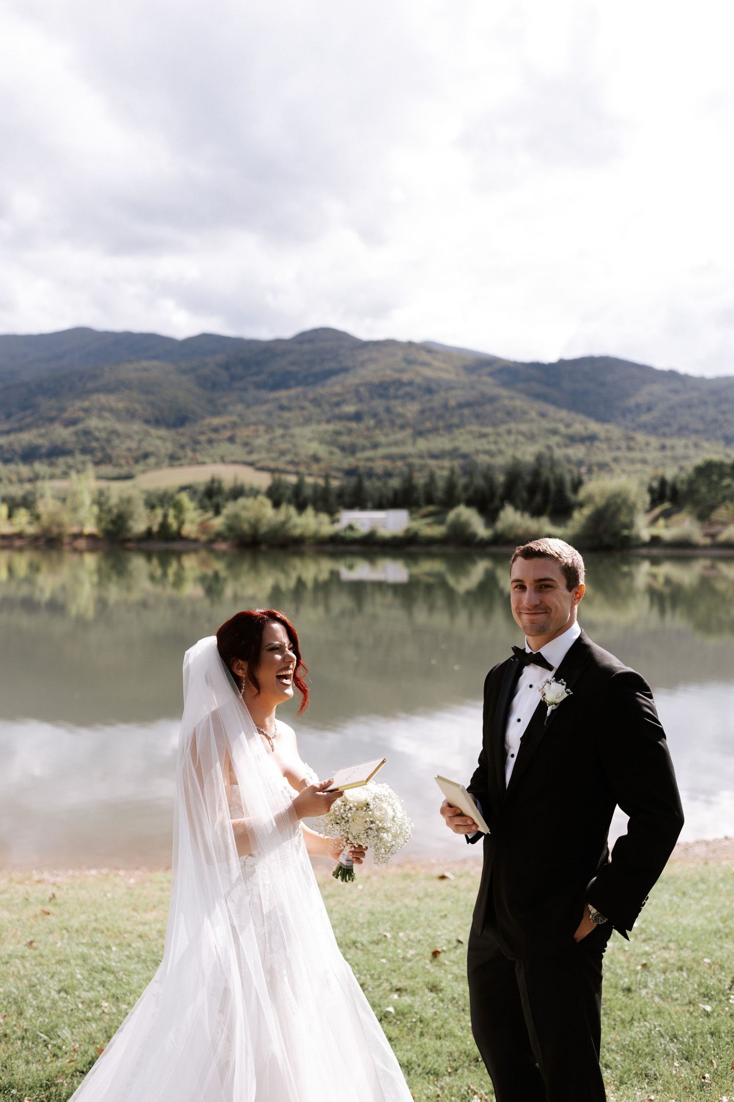A wedding couple shares a joyful moment by a serene mountain lake.