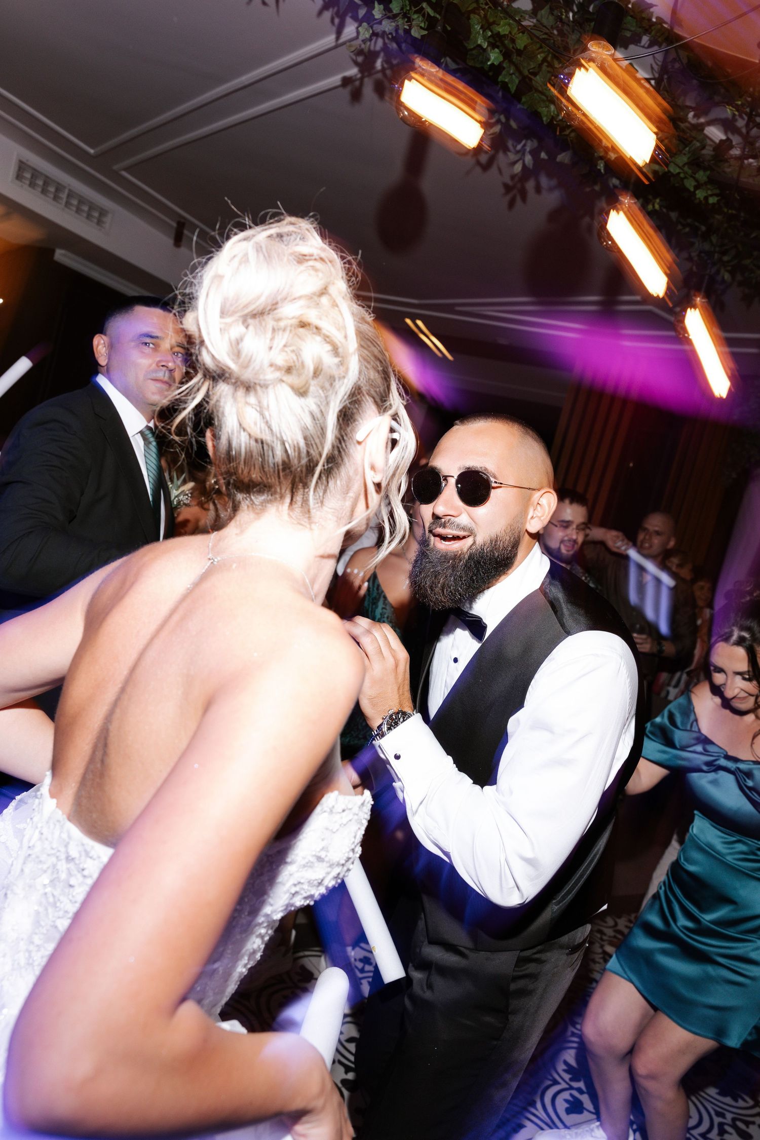 People dancing and celebrating at a lively wedding reception with colorful lighting and a festive atmosphere.