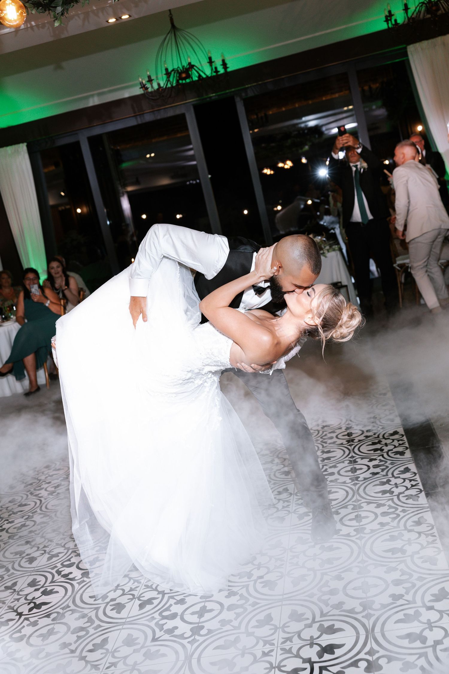 A couple performs a romantic dance dip on a patterned dance floor with green lighting in the background.
