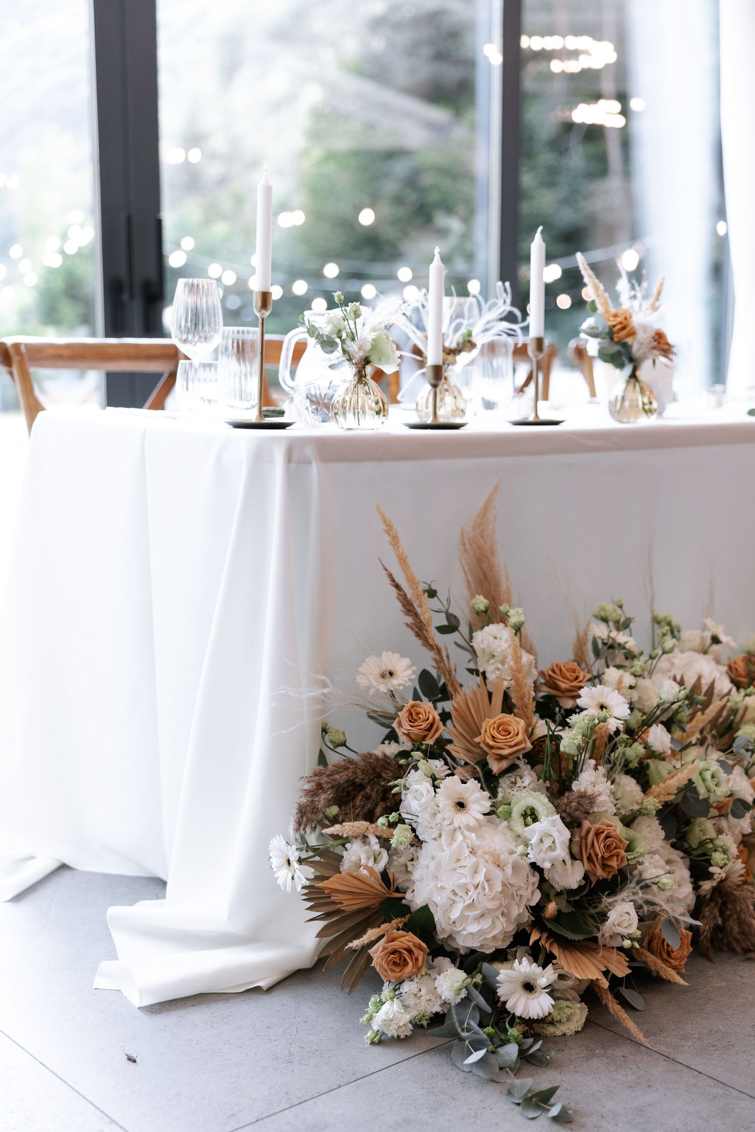 Elegant wedding reception table setting with white and blush floral centerpiece arrangements and delicate glassware.