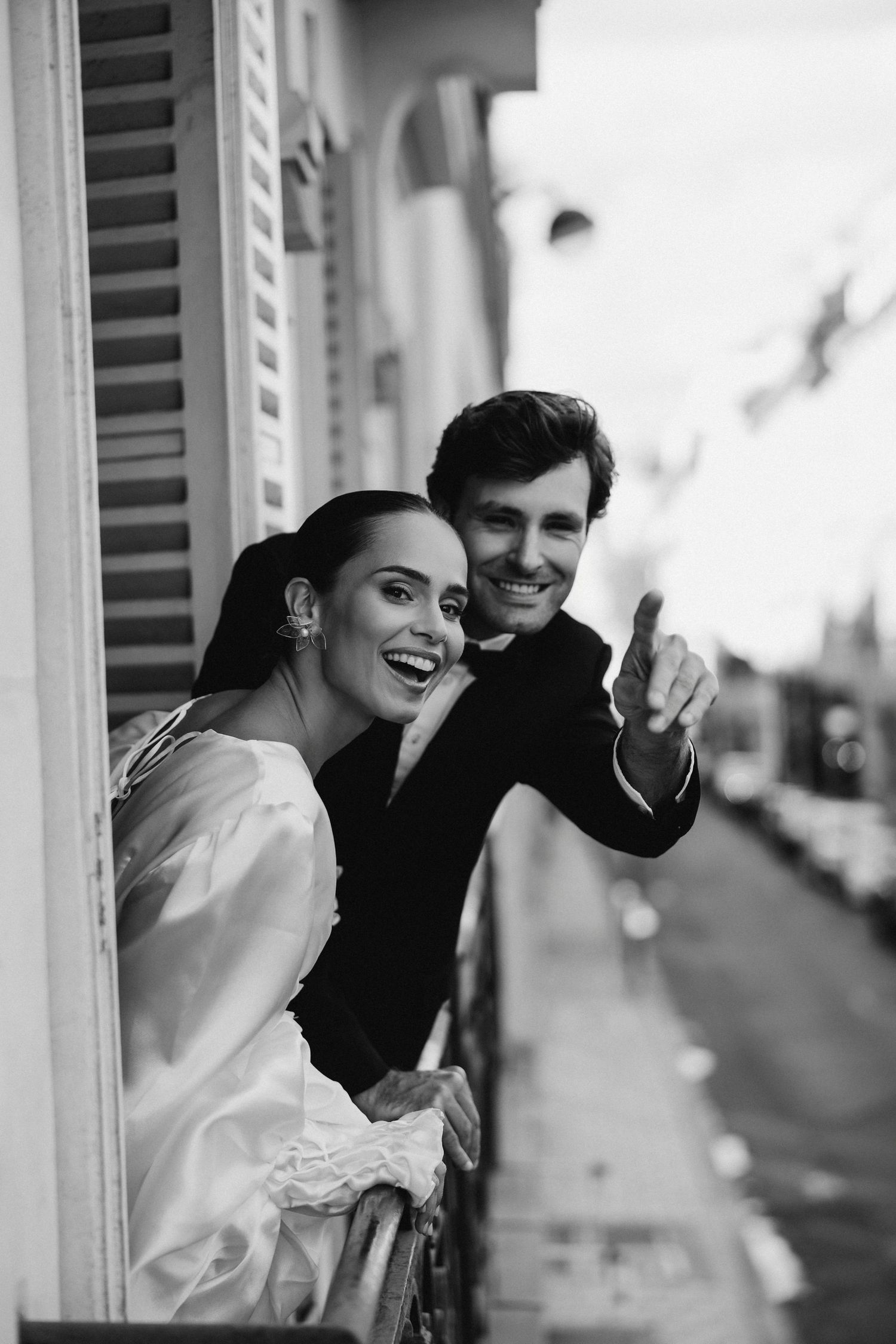 Black and white portrait of couple sharing joyful moment by window shutters.