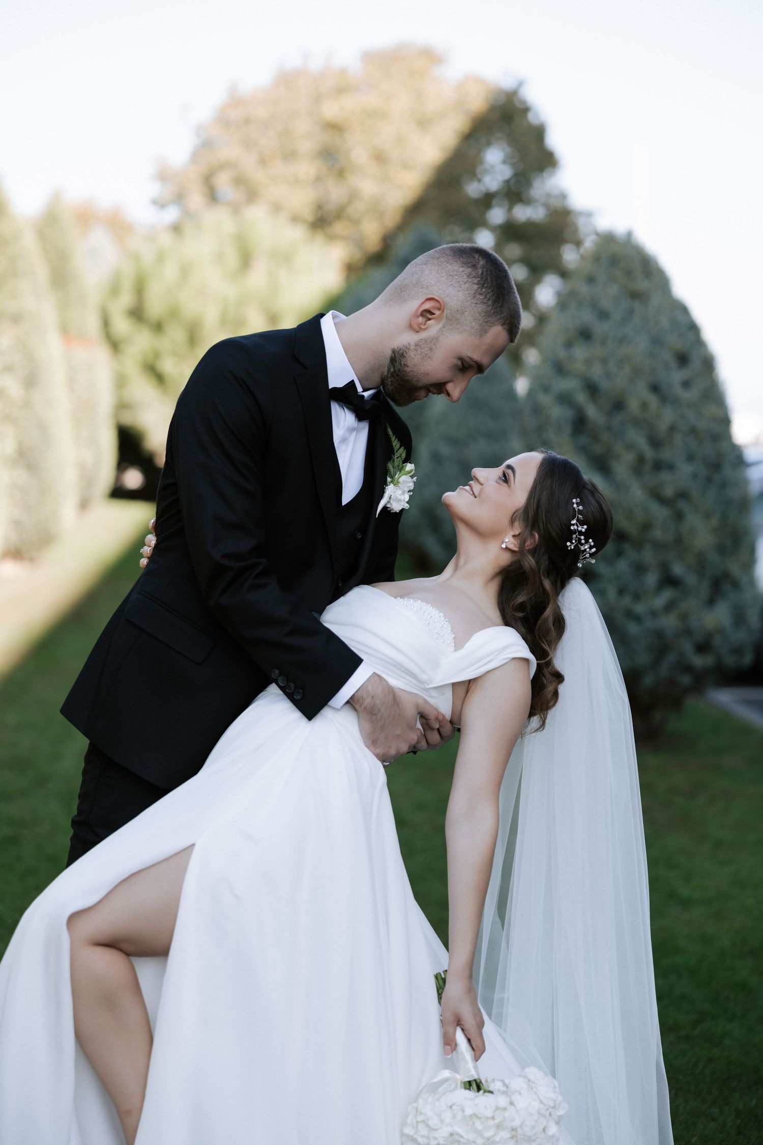 Playful wedding pose with couple in classic attire against garden backdrop.