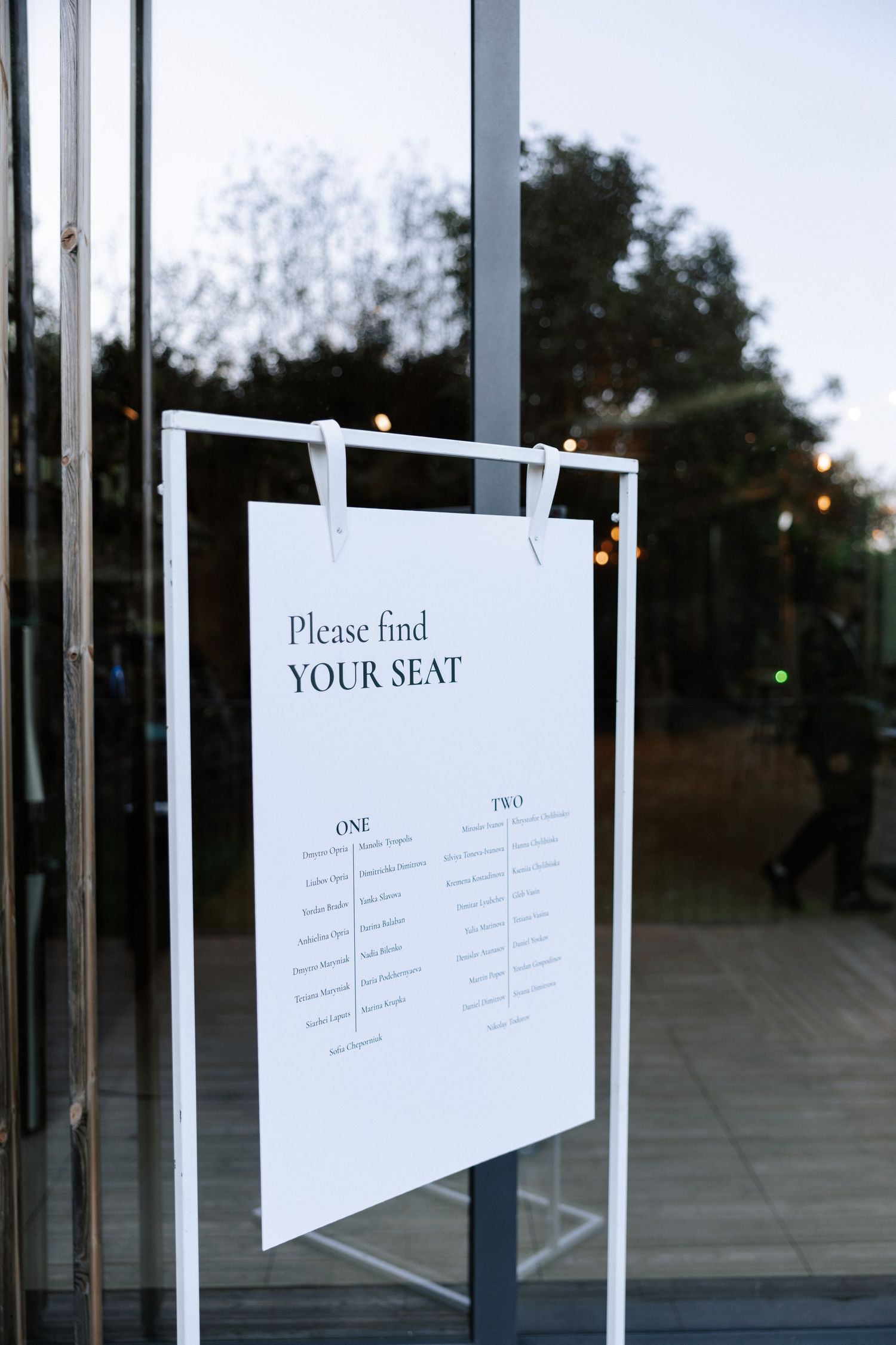 Wedding seating chart displayed on glass door with minimal design.