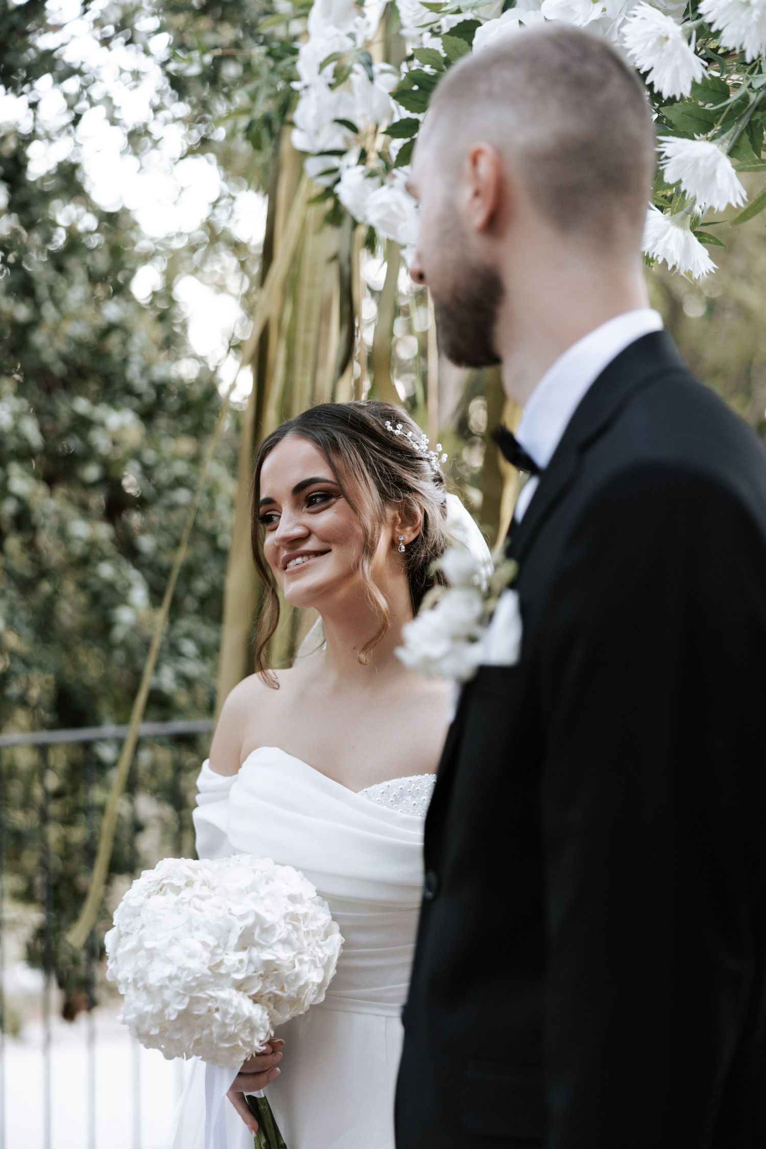 A joyful wedding moment captured outdoors with white floral decorations and natural greenery.
