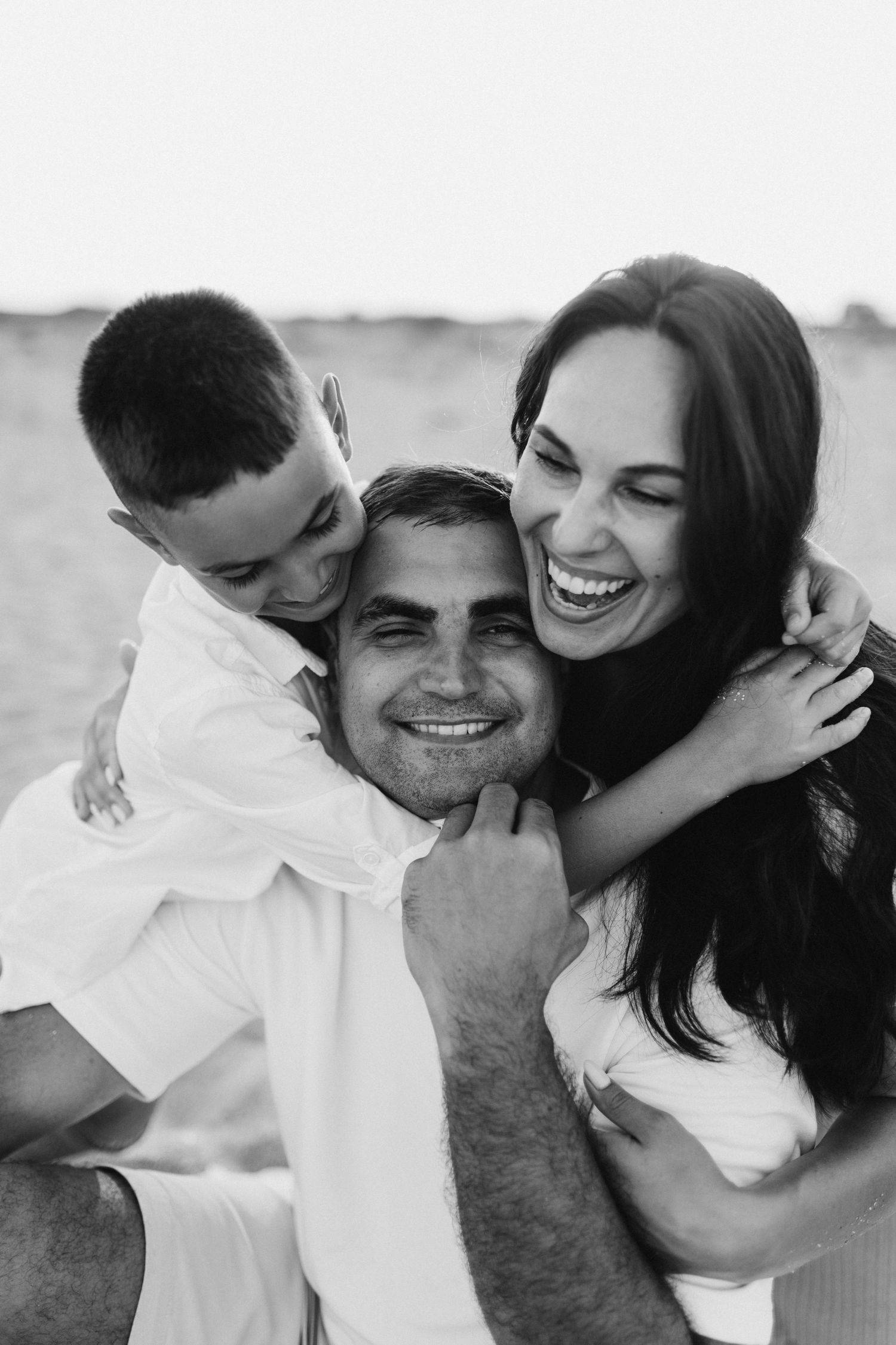 Black and white photo of a joyful family embracing and laughing together outdoors.