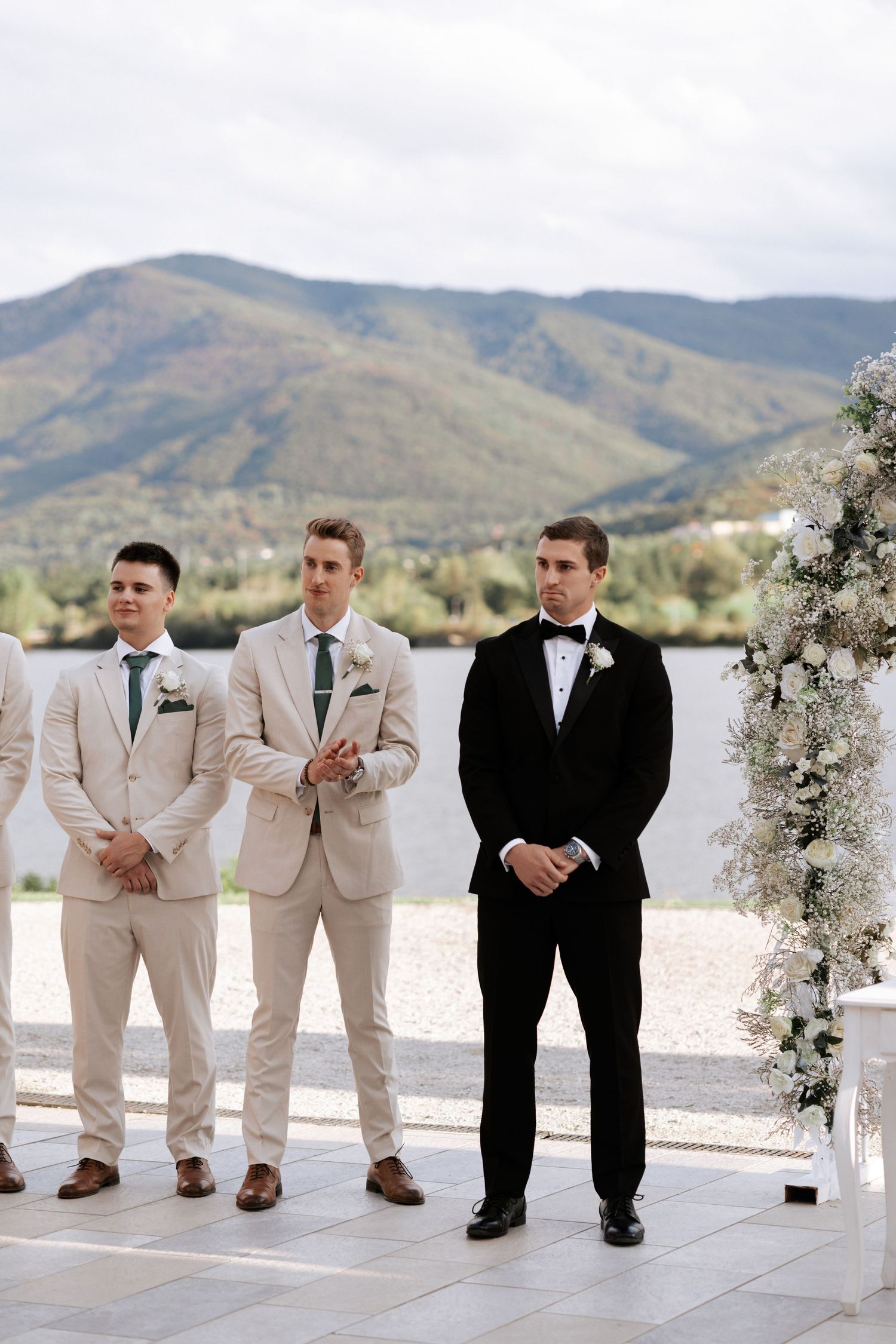 Groomsmen stand at an outdoor wedding ceremony with mountains in the background.