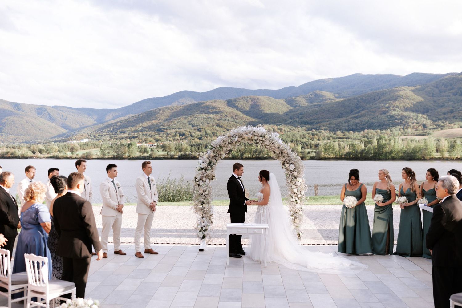 Wedding ceremony overlooking mountains with attendants in white and sage green attire.Wedding photographer Bulgaria
