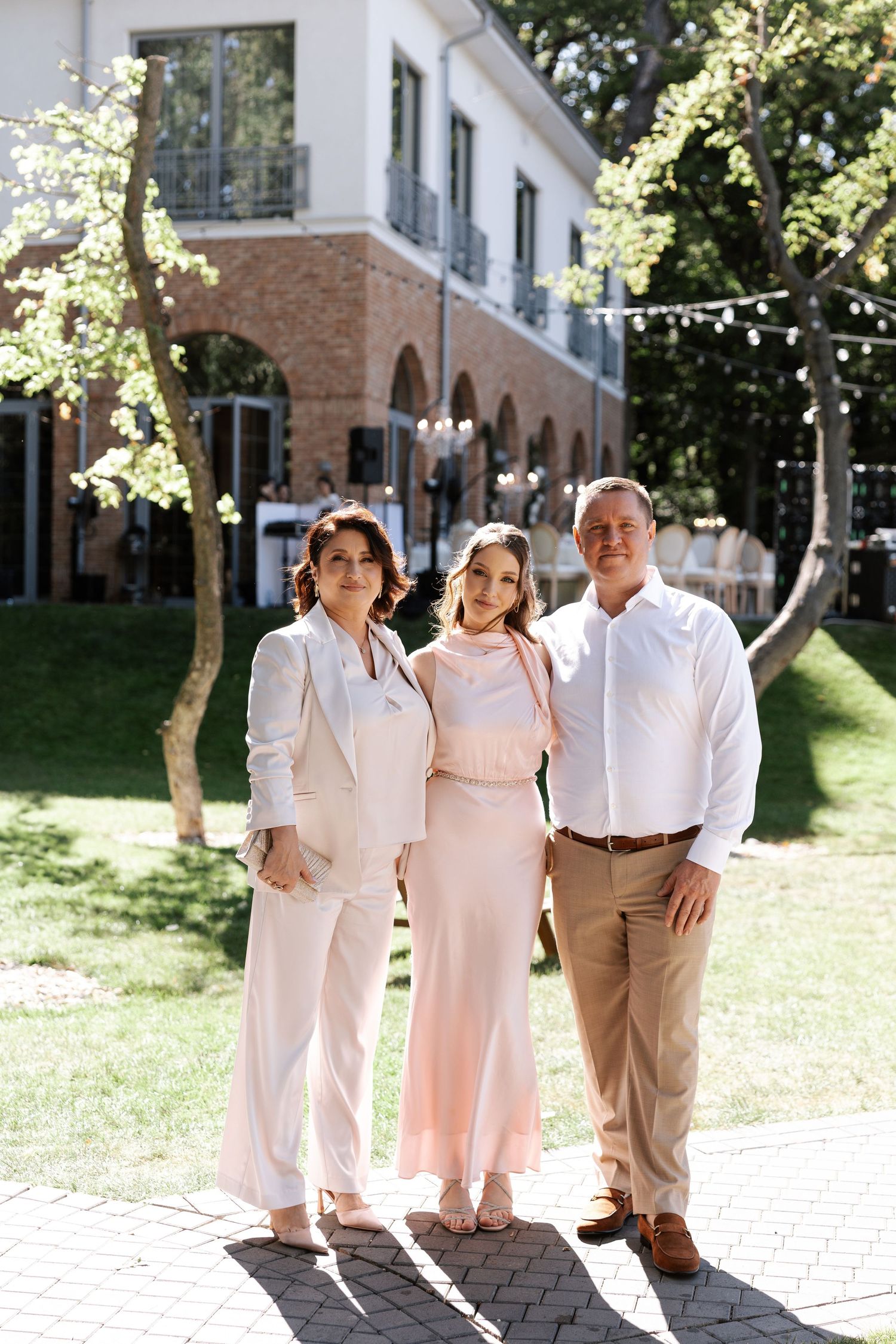 Group photo of wedding guests in light colored attire standing together outdoors.