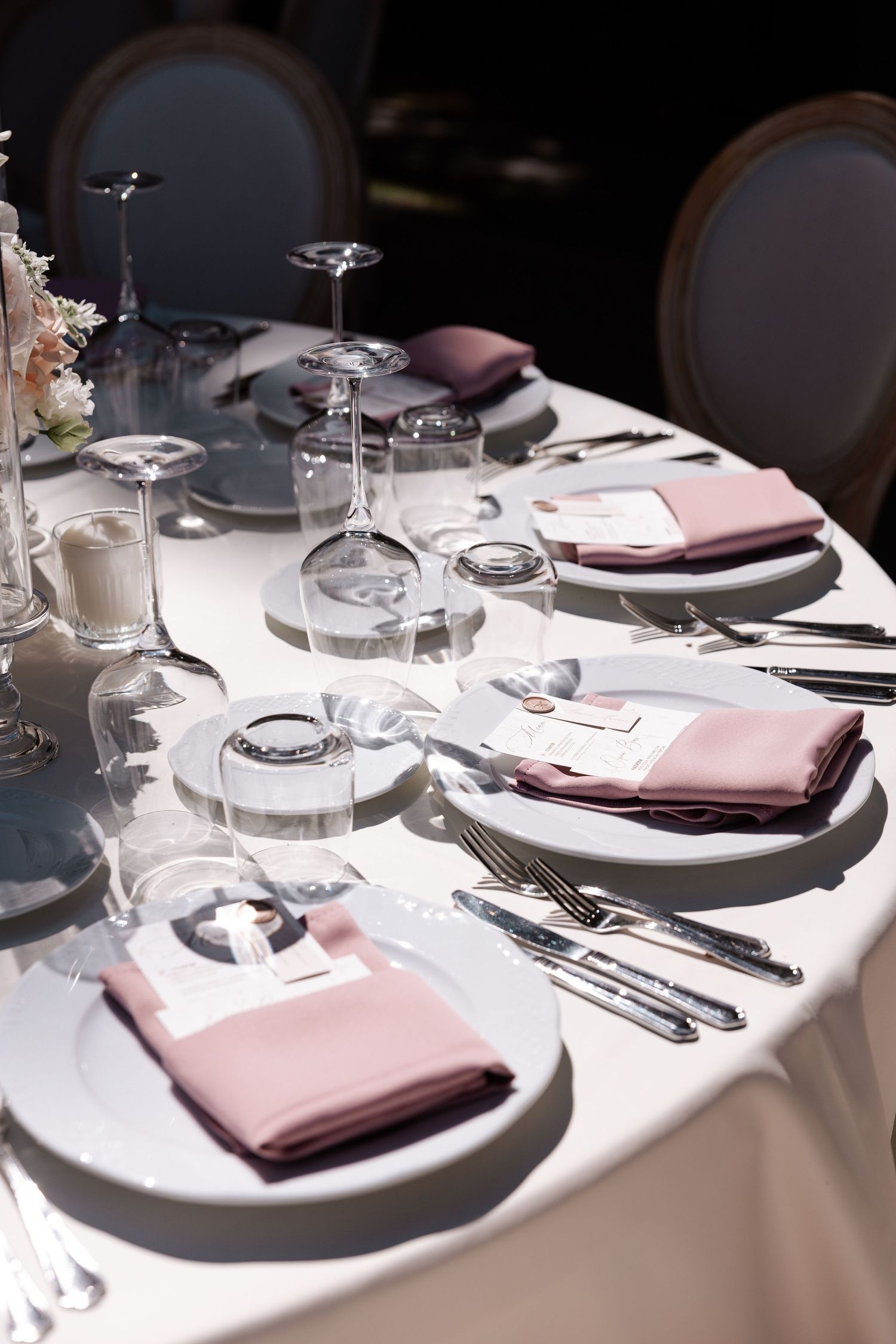 Sunlit wedding table setting with pink napkins and crystal stemware.