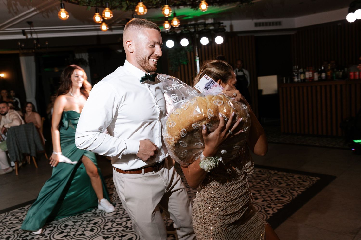 People dancing together at a wedding reception with string lights and stage lighting overhead.