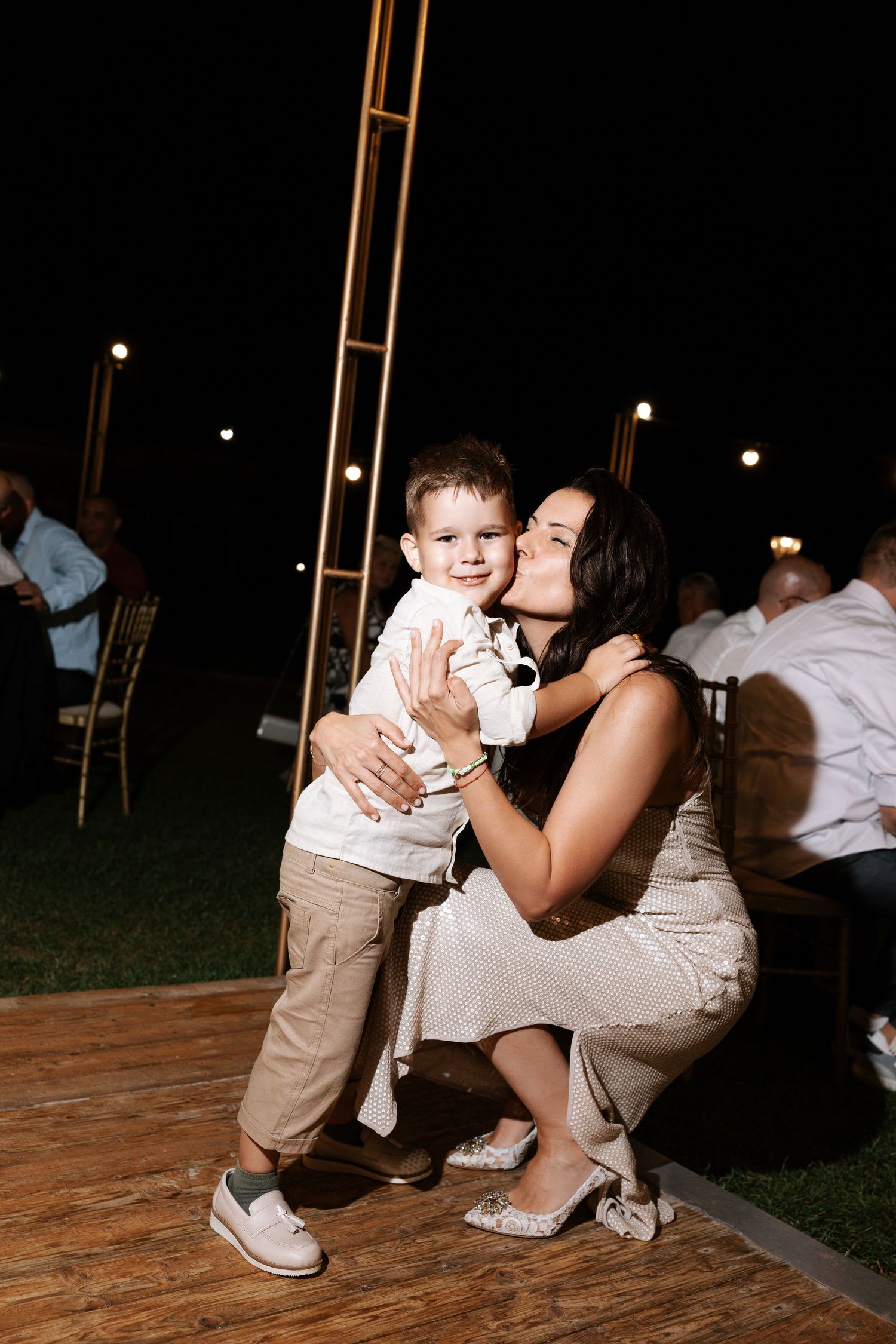 A tender moment between parent and child dancing together on a wooden floor at an evening celebration.