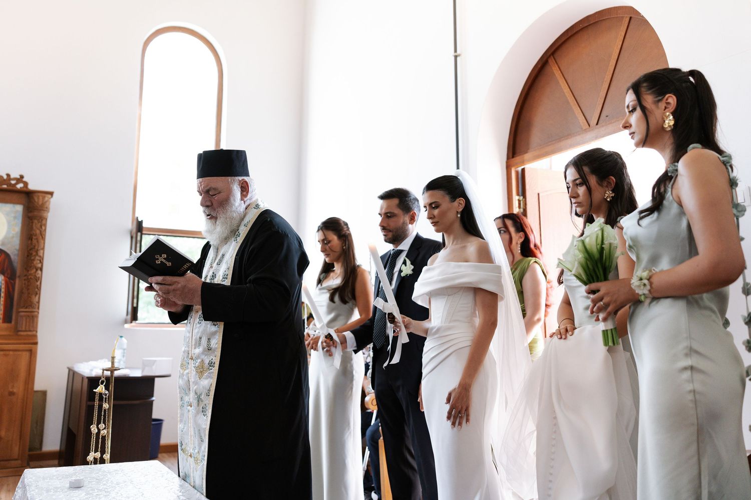 A panoramic view of a wedding ceremony with people in formal attire standing in a line against a white wall.