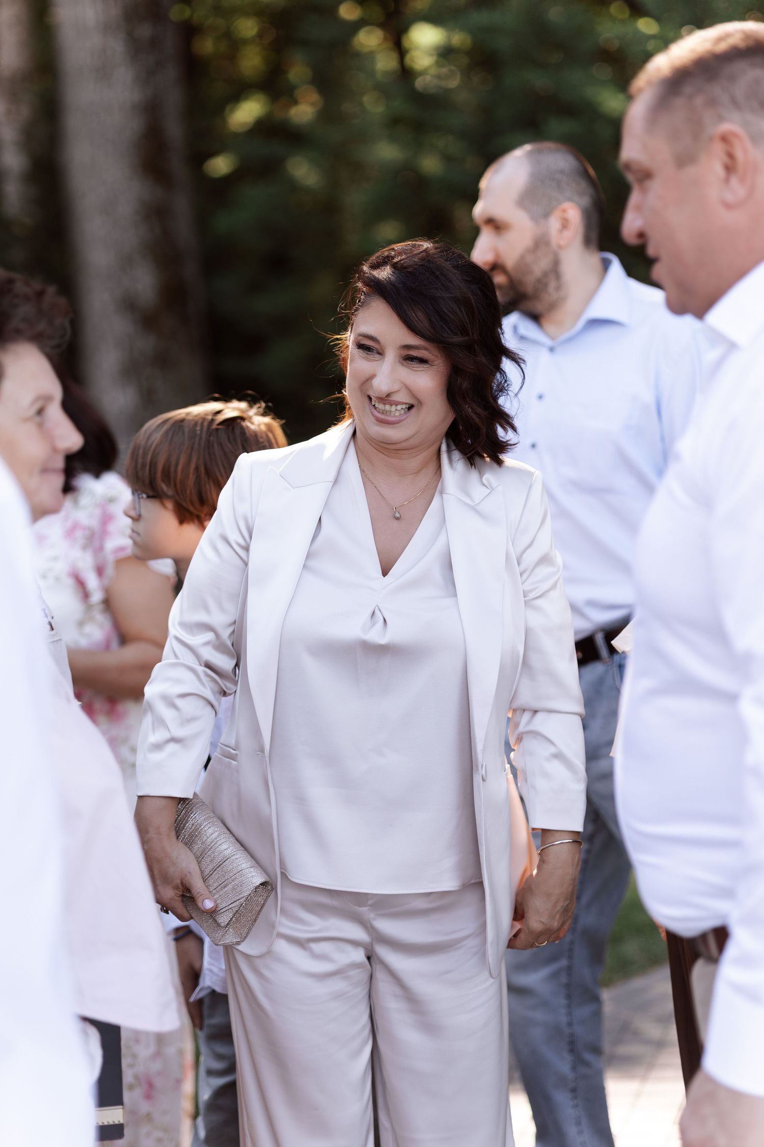 Wedding guests in white and beige attire gathered outdoors for a celebration.