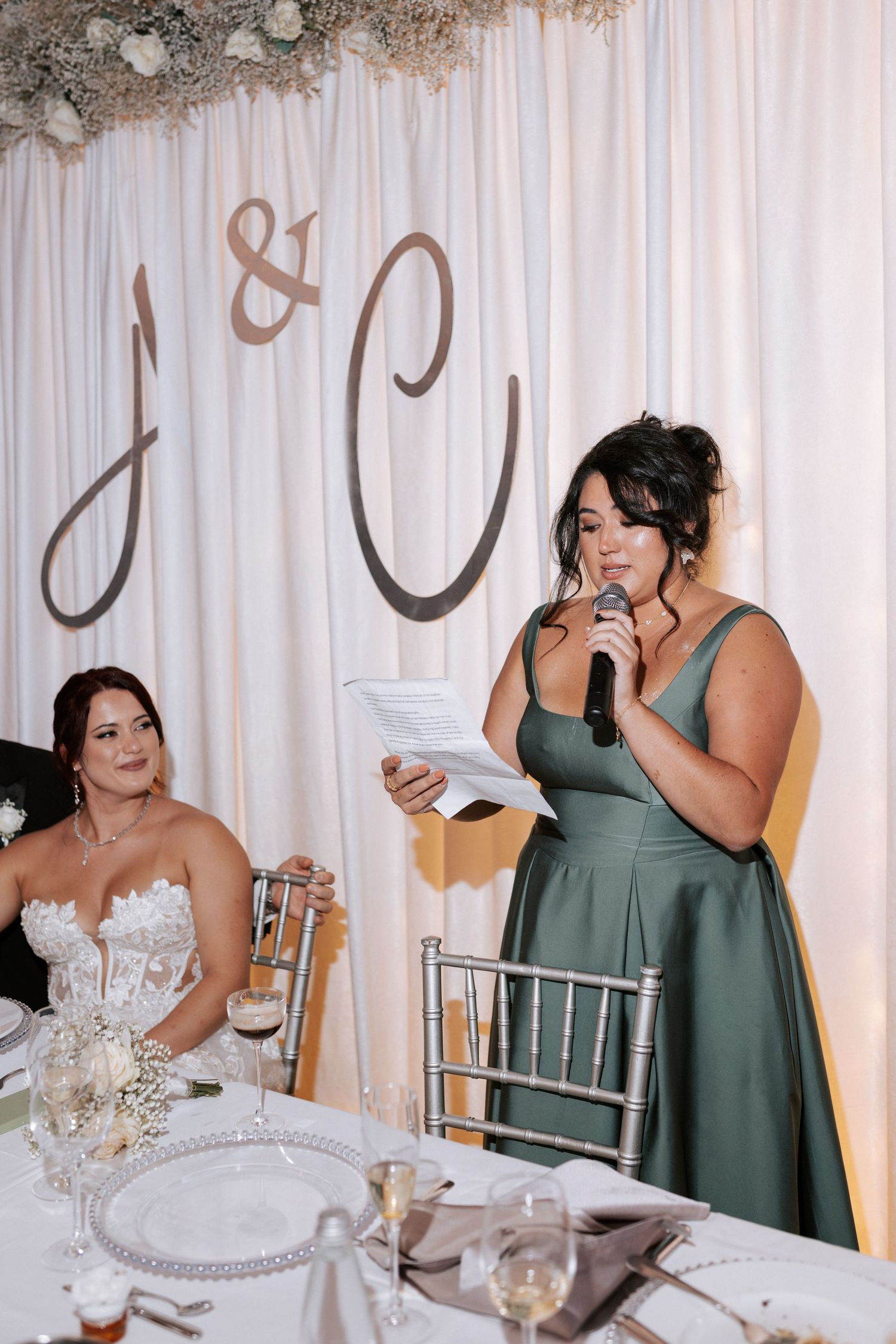 Wedding speech being delivered at decorated head table with monogram backdrop.